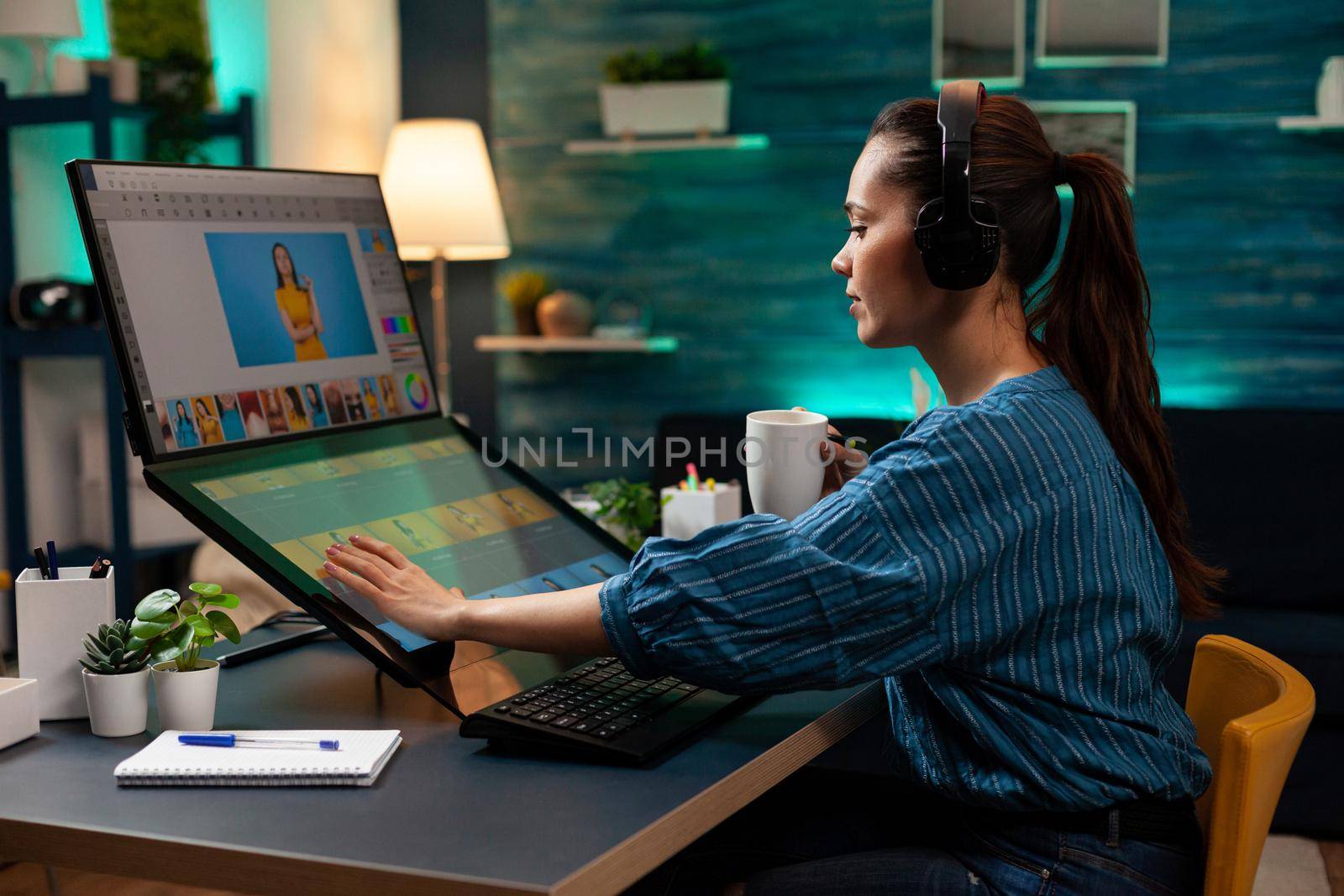Graphic software editor with headphones working on photography project using touchpad computer monitor sceen display. Woman at workplace doing photo retouching with modern interface