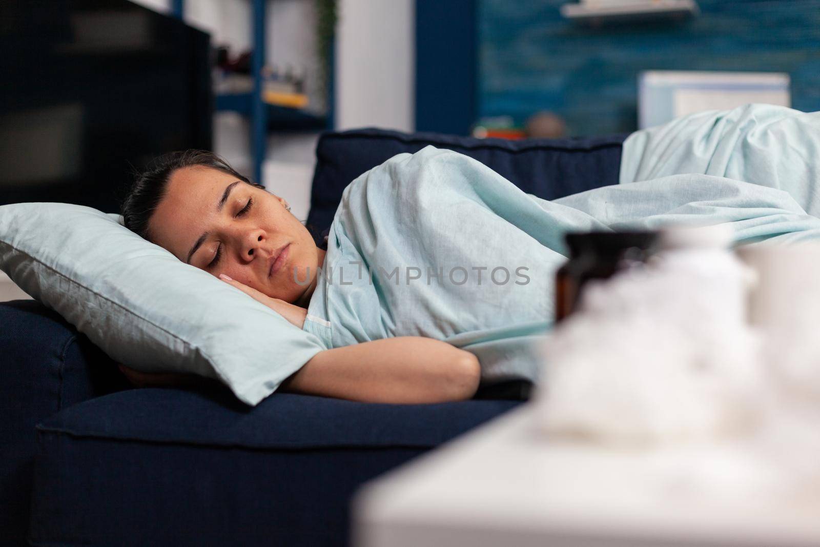 Sick caucasian woman with sickness sleeping in her home. Taking treatment for cold flu illness symptoms and resting in bed. Unwell tired young adult sleeping under the blanket.