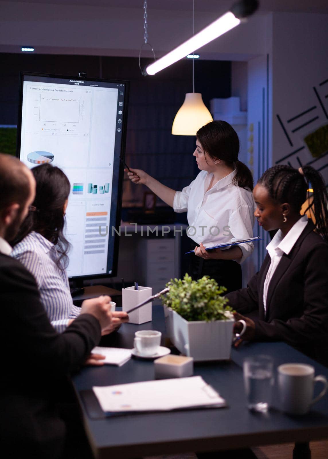 Executive manager woman explaining management statistics working at company strategy overtime in office meeting room. Diverse multi-ethnic businesspeople teamwork brainstorming ideas in evening.