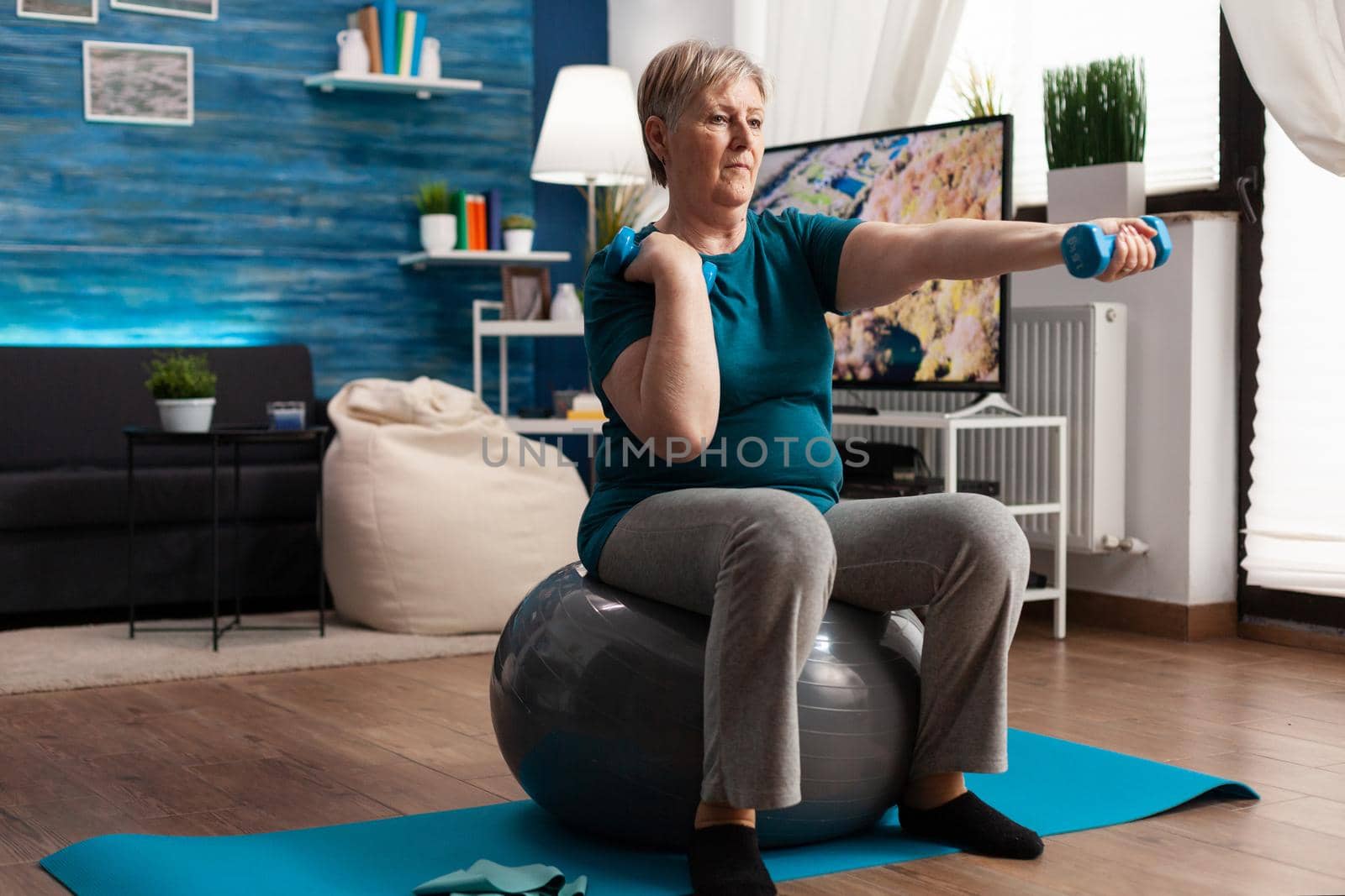 Athletic pensioner in sportswear watching online aerobic workout using tablet sitting on swiss ball by DCStudio