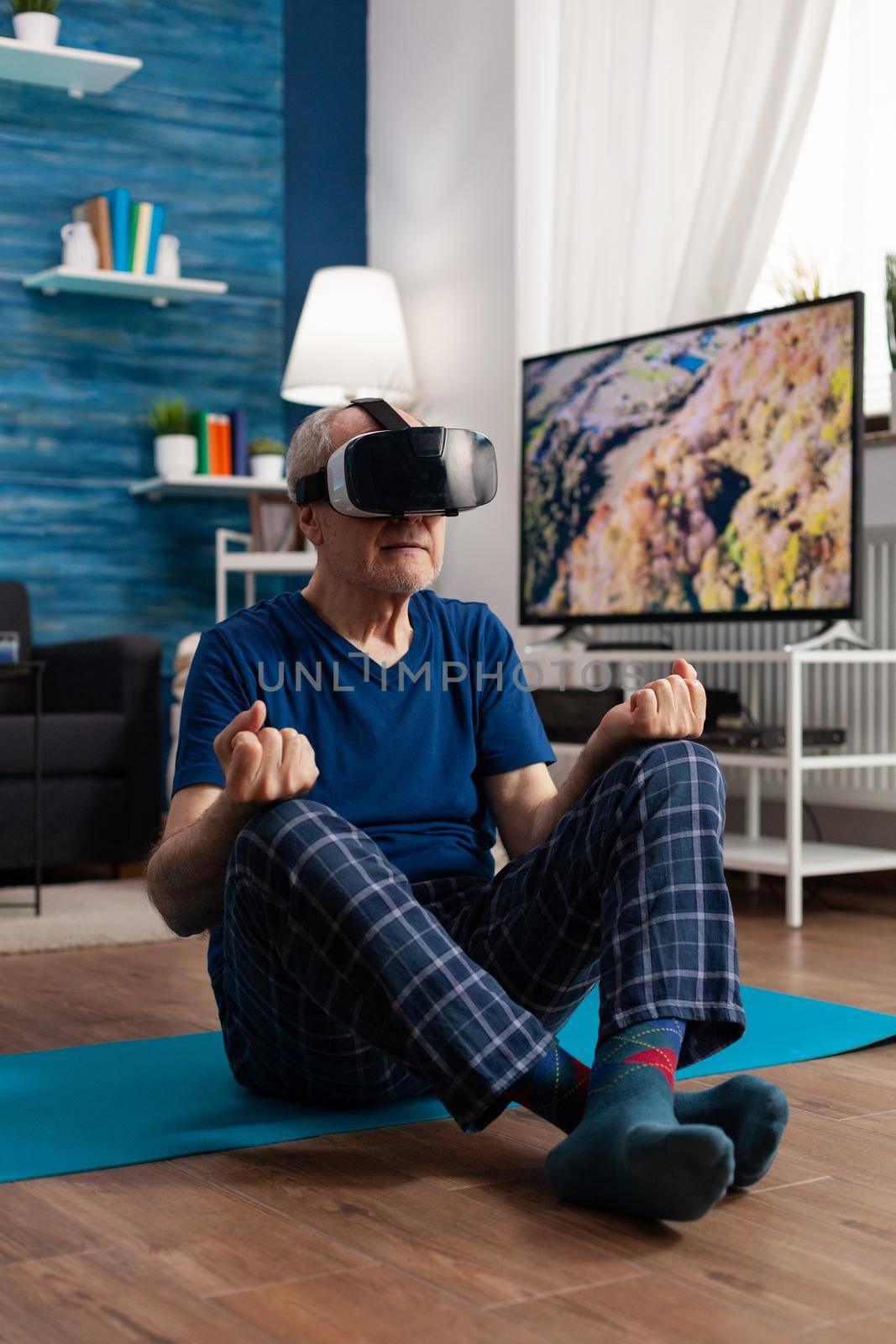 Senior man wearing virtual reality headset practicing meditation exercise sitting on yoga mat by DCStudio