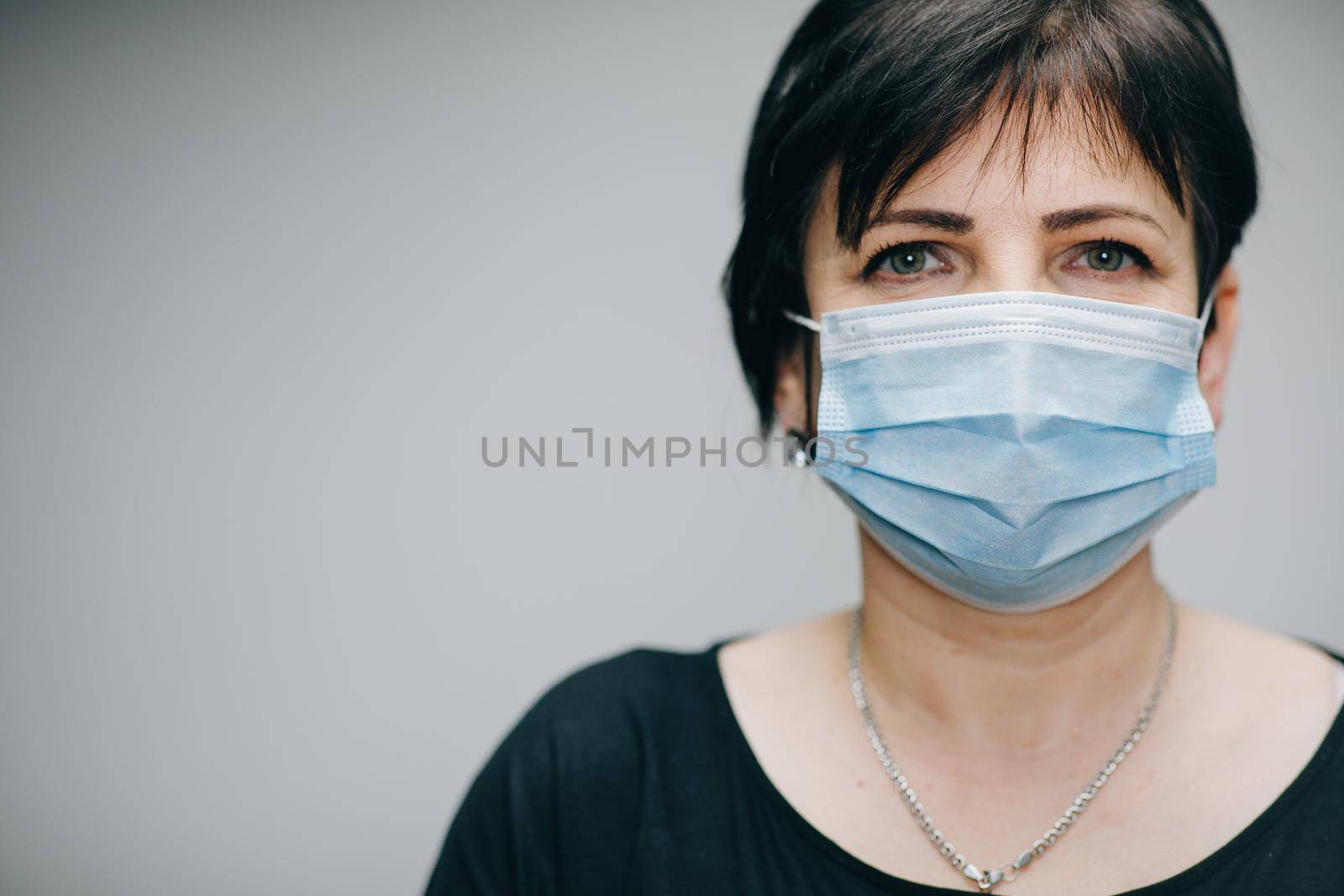 Senior Woman Takes on Medical Mask. Breathes deeply and looking at camera on grey background. Health care and medical concept.