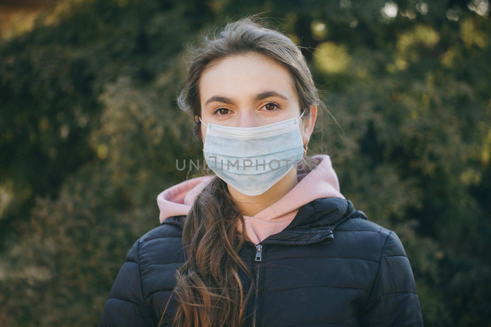 Sick girl wearing protection during pandemic. Pretty young Caucasian girl taking on medical mask outdoor. Girl Wearing Medical Mask During Coronavirus COVID-19 Epidemic. by uflypro