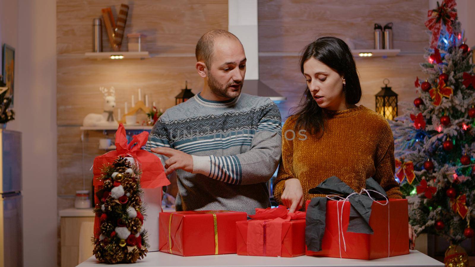 Man bringing presents to sort for family on christmas eve. Couple preparing with gift boxes, ribbon and wrapping paper for holiday celebration. Festive people celebrating winter season