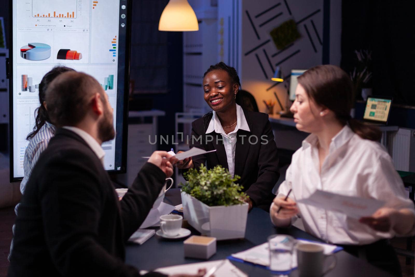 Diverse multi-ethnic businesspeople overworking late at night analyzing management ideas solving company statistics. Workaholics teamwork working in office meeting room in evening..