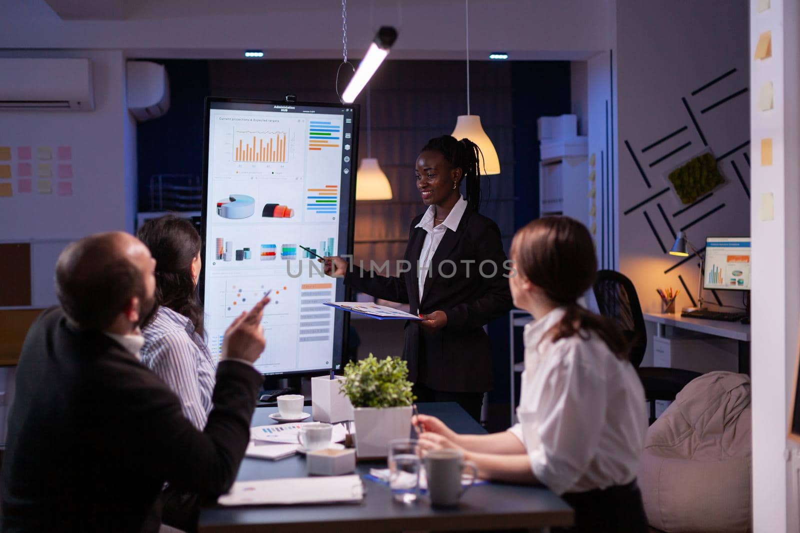 Workaholic african american leader standing in front of presentation monitor explaining marketing project by DCStudio