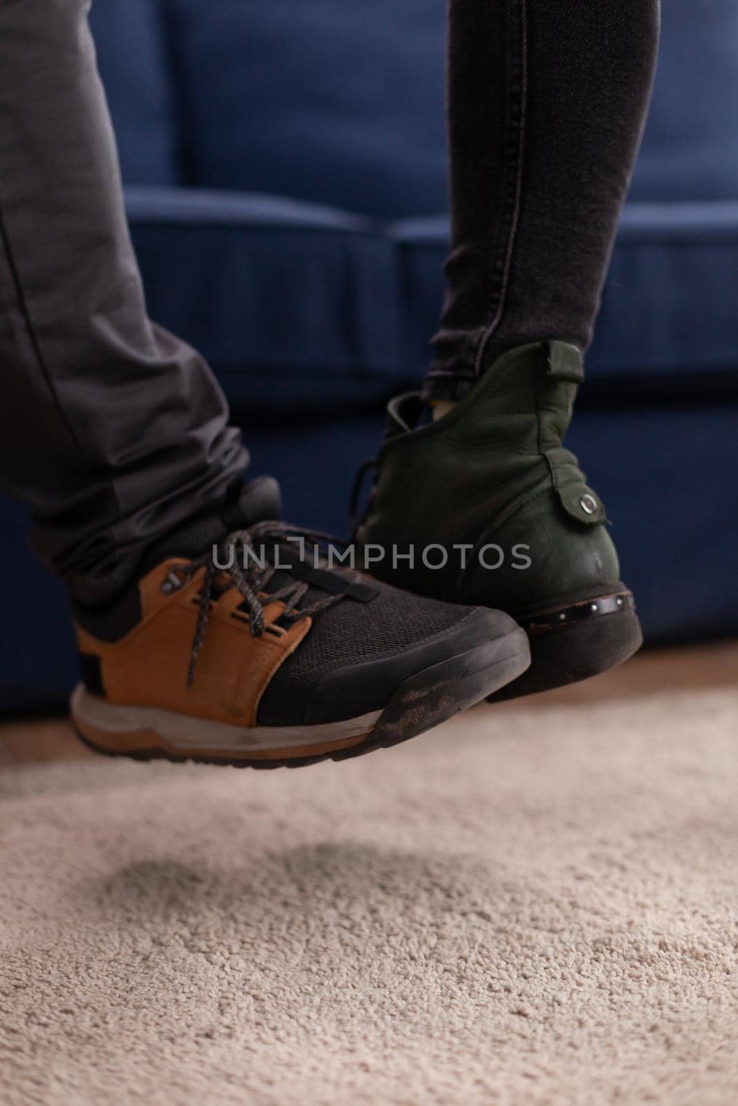 Happy cheerful friends touching feet keeping social distancing greeting eachother wearing face mask preventing spread of coronavirus holding beer bottles in apartment living room. Conceptual image.