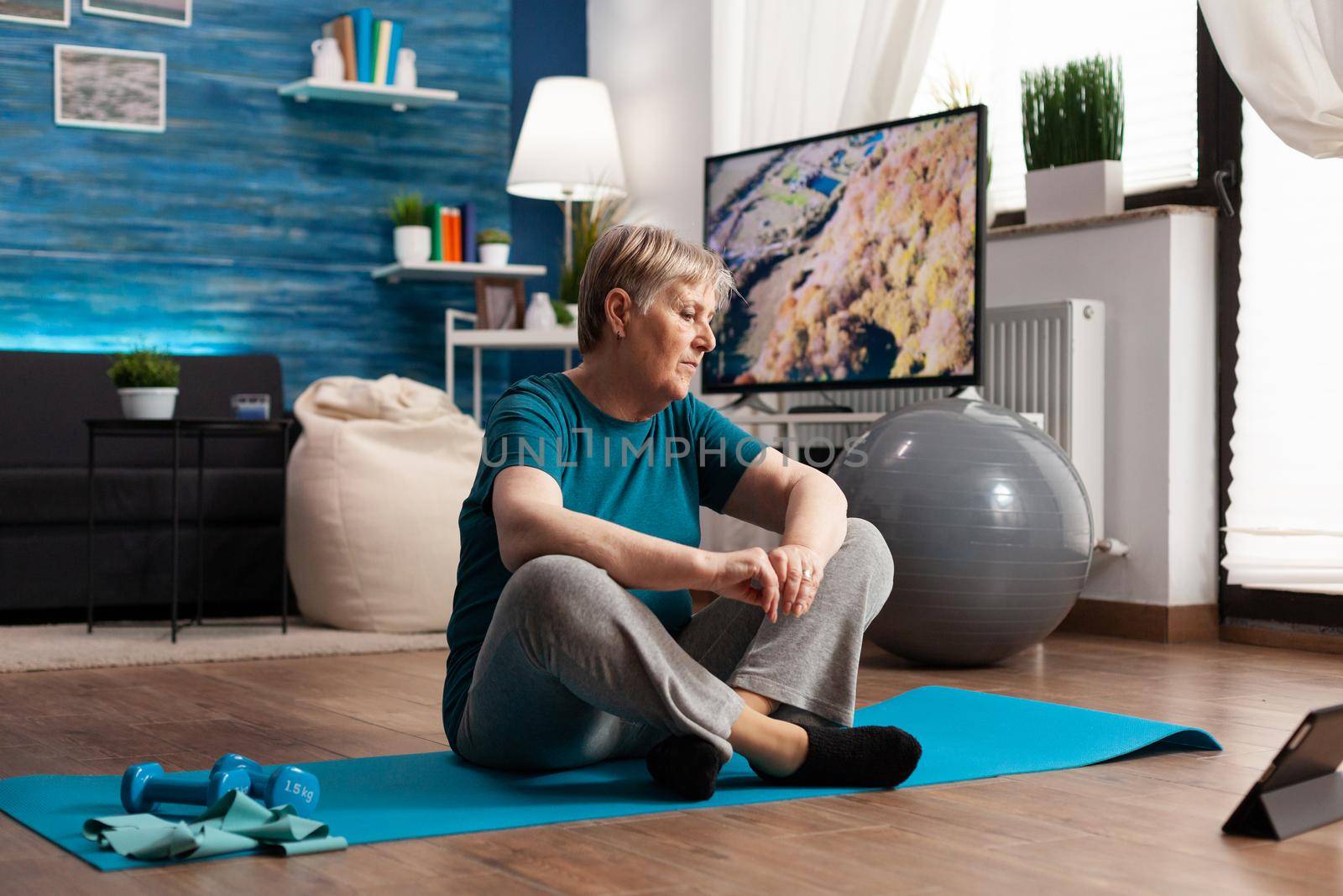 Senior woman sitting in lotus position on yoga mat training body muscles slimming weight by DCStudio