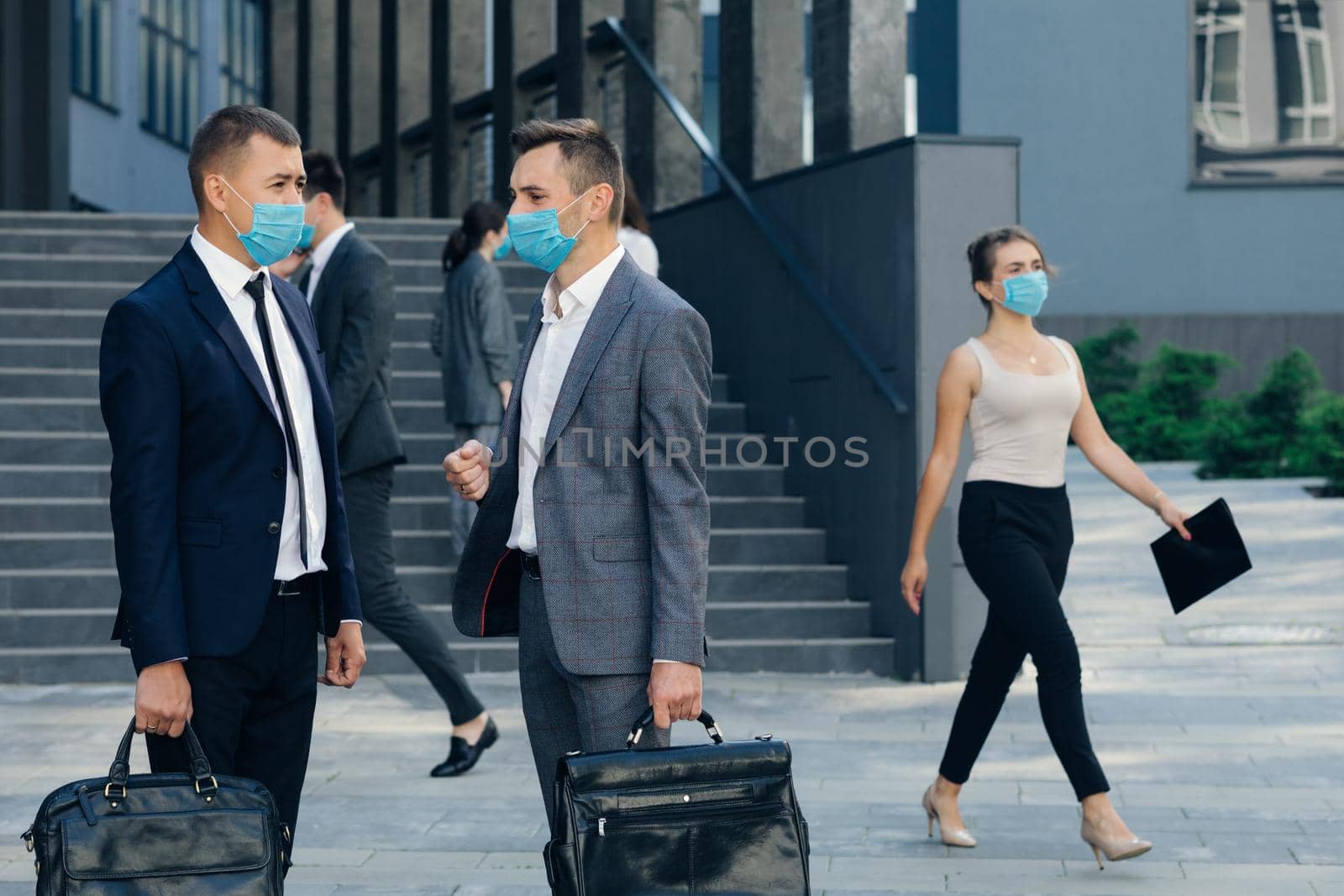 Two Employees Co-workers Manager in Protective Mask Discussing Outside Office Building. Confident Man Explaining Something to Male Colleague by uflypro