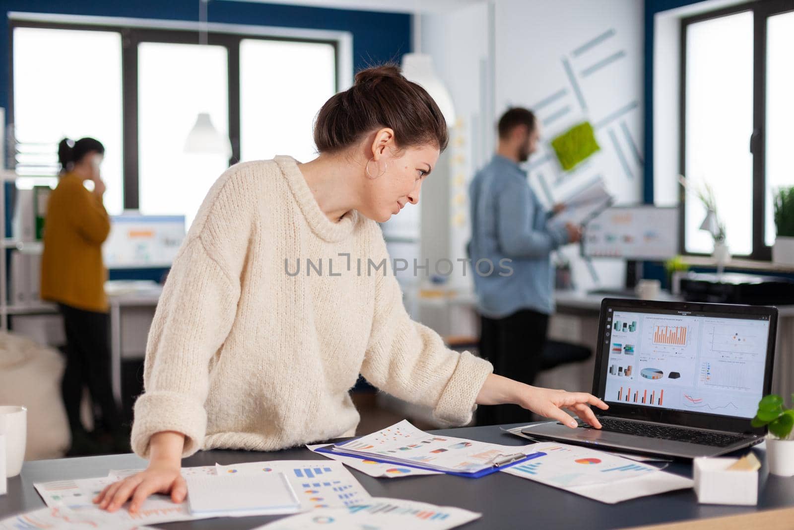 Busy businesswoman employee concentrated on company charts scrolling on laptop. Successful corporate professional entrepreneur online internet statistics. Executive entrepreneur, manager leader standing working on projects with diverse colleagues.