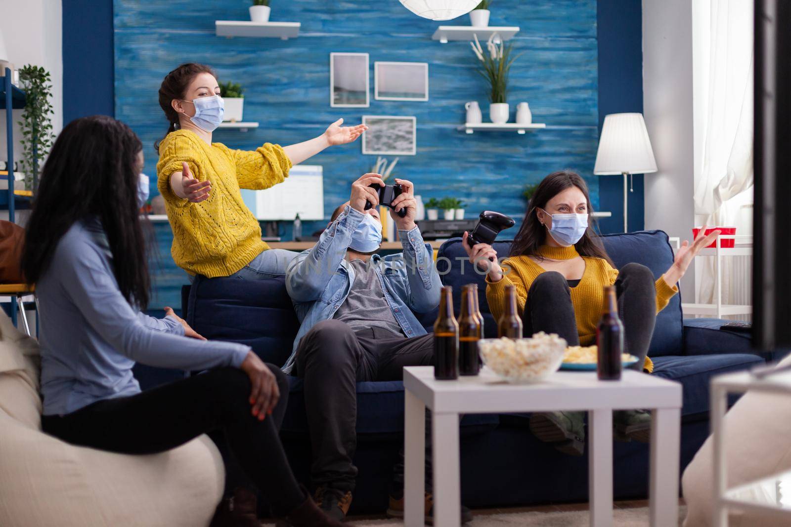 Happy cheerful woman screaming after wining gaming competiton with multiethnic friends in home living room with face mask preventing coronavirus spreading in time of global pandemic.