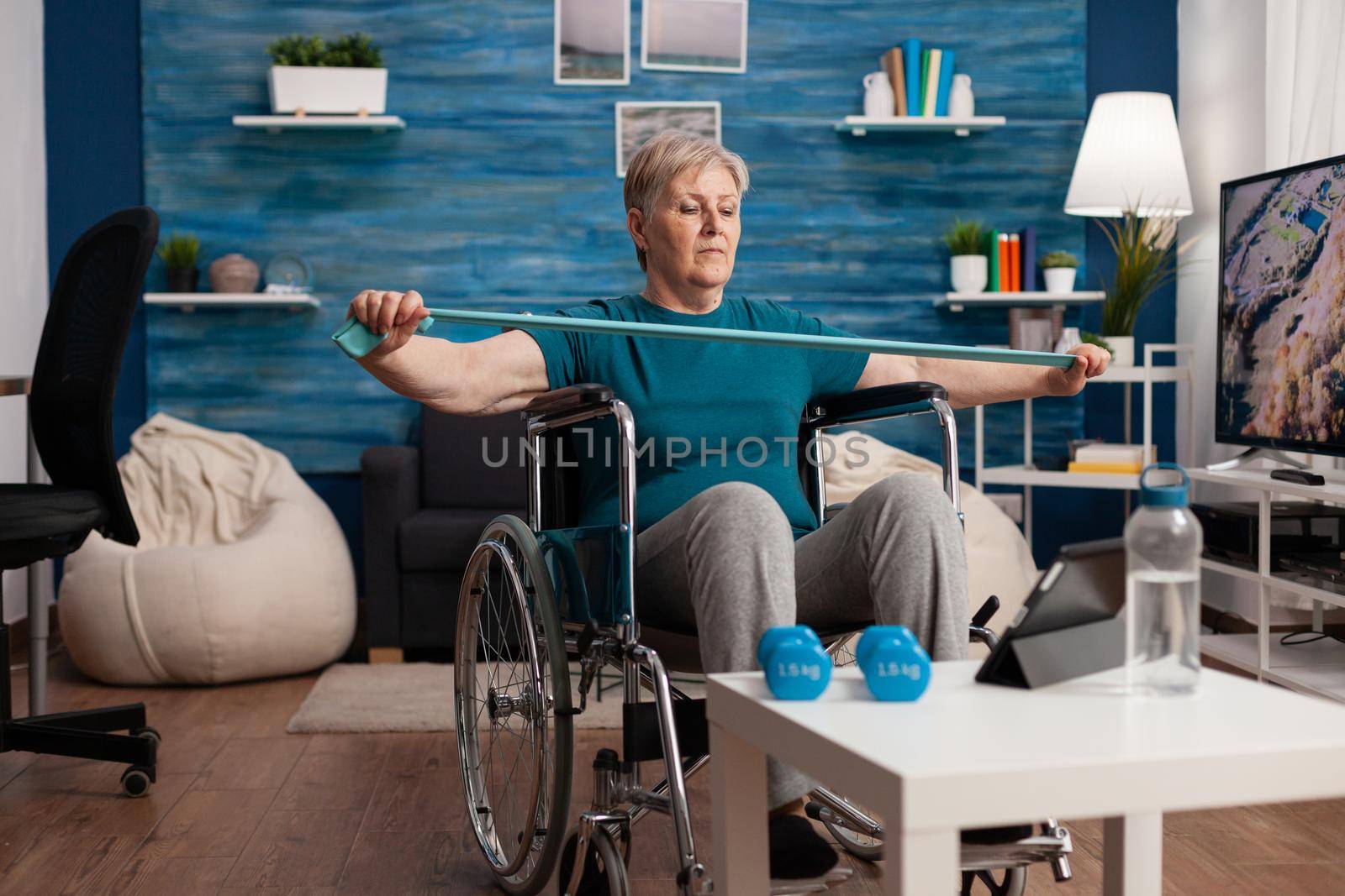 Invalid old woman in wheelchair stretching arm resistance training body muscle using elastic band by DCStudio