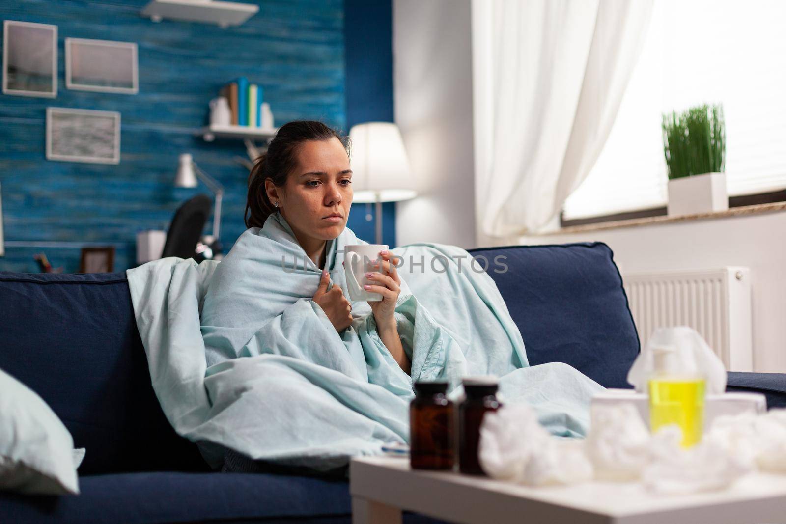Person with sickness disease at home taking treatment for cold and flu sitting on sofa. Seasonal symptoms and cough, holding mug with tea or medicine disease treatment. Throat unwell healthcare