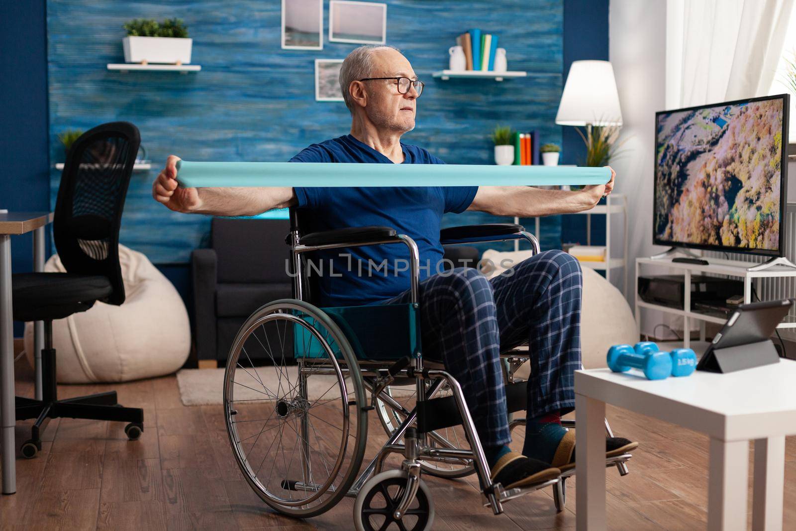 Disabled senior man in wheelchair training with elastic band exercising body workout by DCStudio