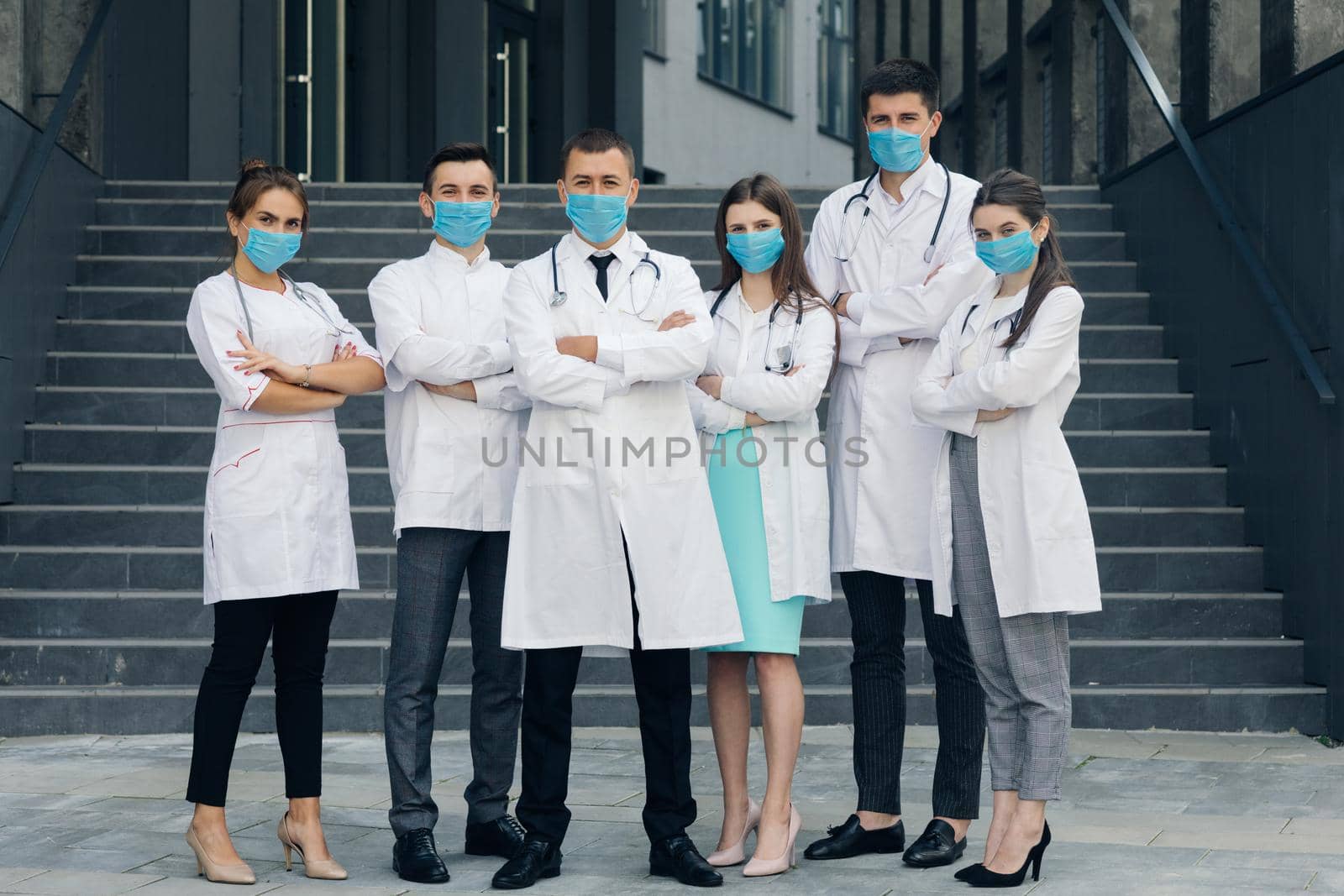 Group of doctors with face masks looking at camera, corona virus concept. Confident team of doctors in face masks standing with their arms folded and looking at camera by uflypro