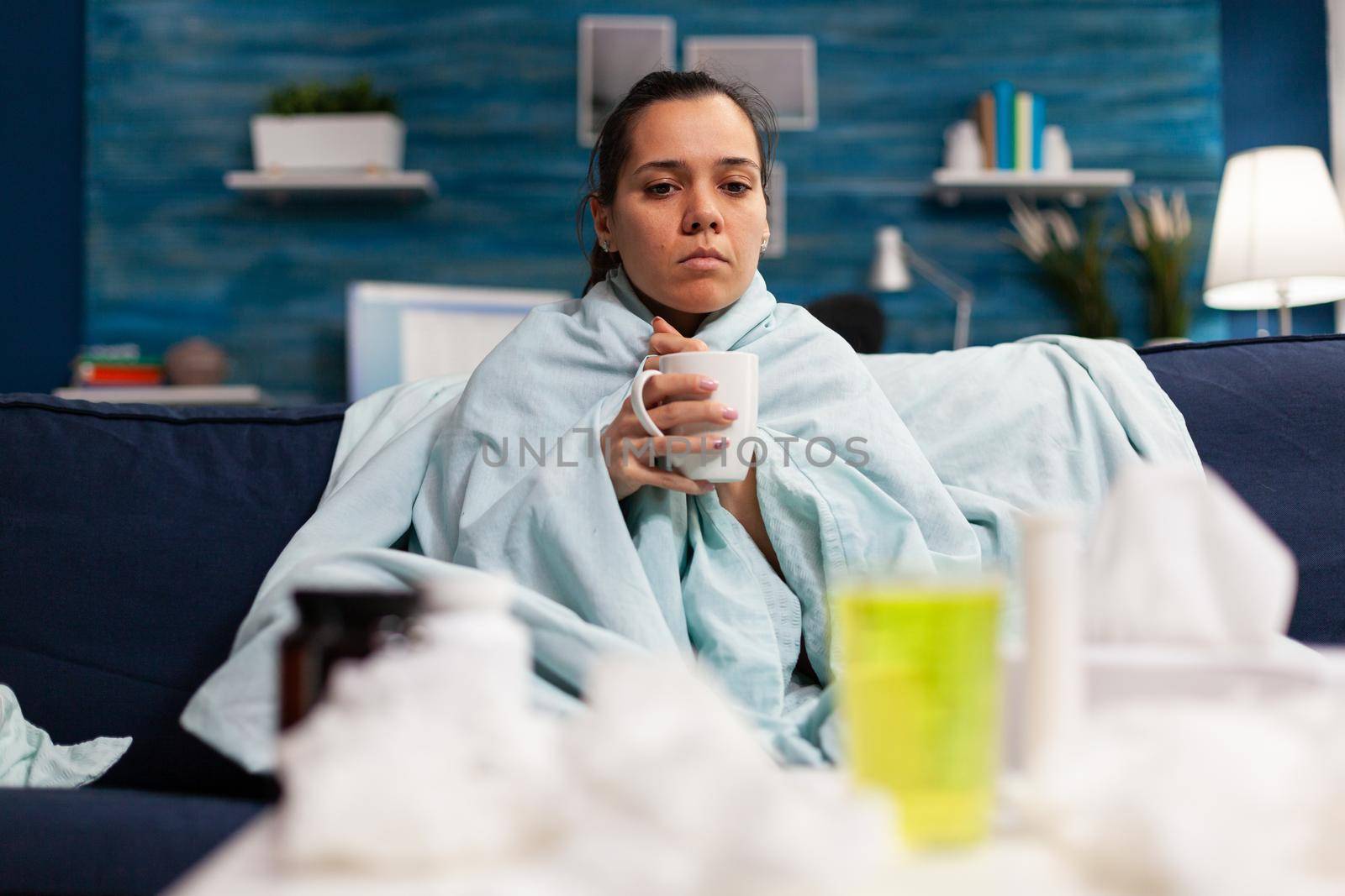 Woman with flu sitting at home drinking hot tea feeling sick. Person with temperature taking medicine for health virus infection, adult with disease pain headache