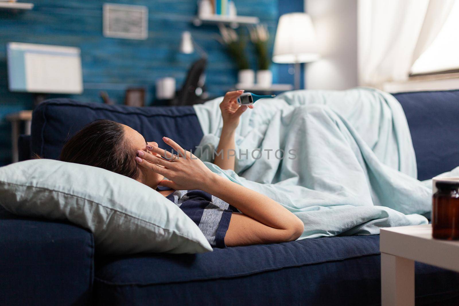 Sick woman measuring temperature with thermometer at home by DCStudio