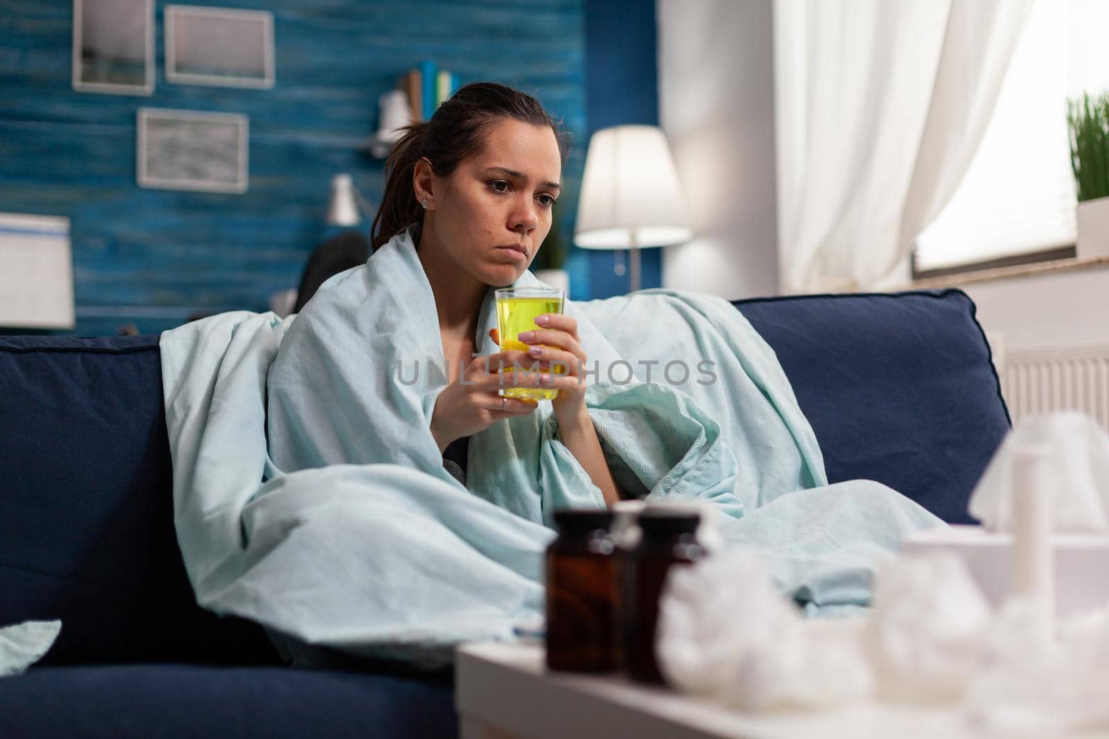 Caucasian woman sitting at home taking medicine for virus infection while feeling sick. Adult with fever cold and flu, seasonal symptoms in bed with cough and throat pain.