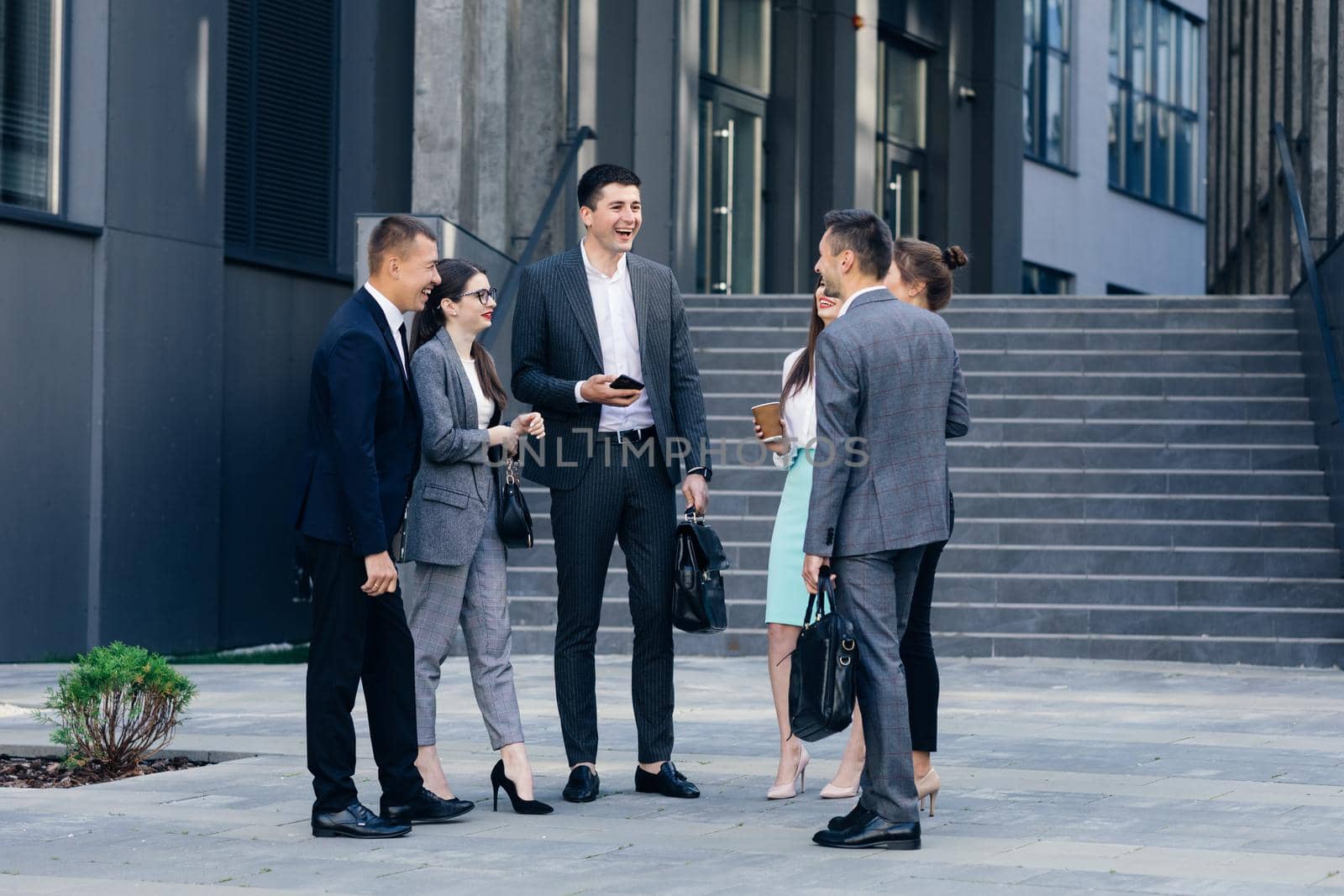 Male and Female Business People Discuss Business. Group of six young caucasian business people men and women meeting discussing outside office building.