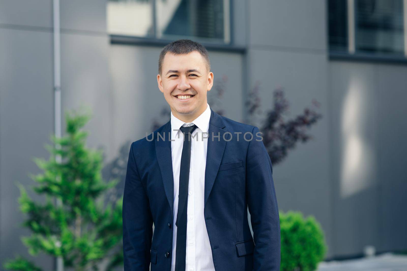 Handsome smiling confident businessman portrait. Modern businessman. Confident young man in suit looking away while standing outdoors with cityscape in the background.