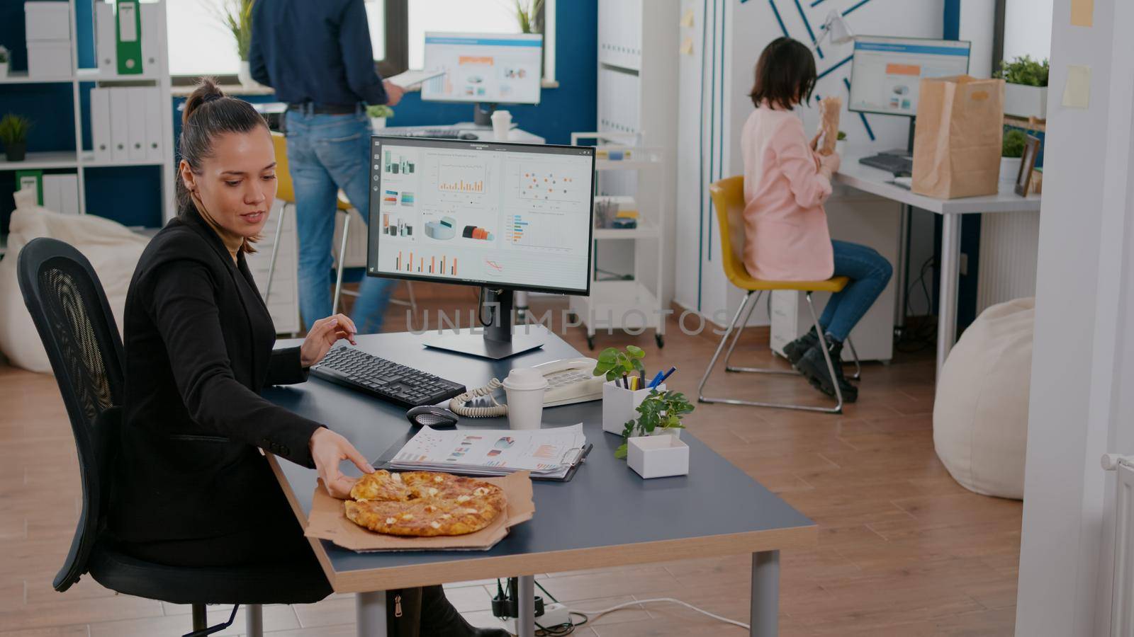 Businesswoman on lunch break at her table eating pizza fastfood delivery. Takeaway delivery meal order package delivered at workplace office. Takeout food at lunchtime eating at desk