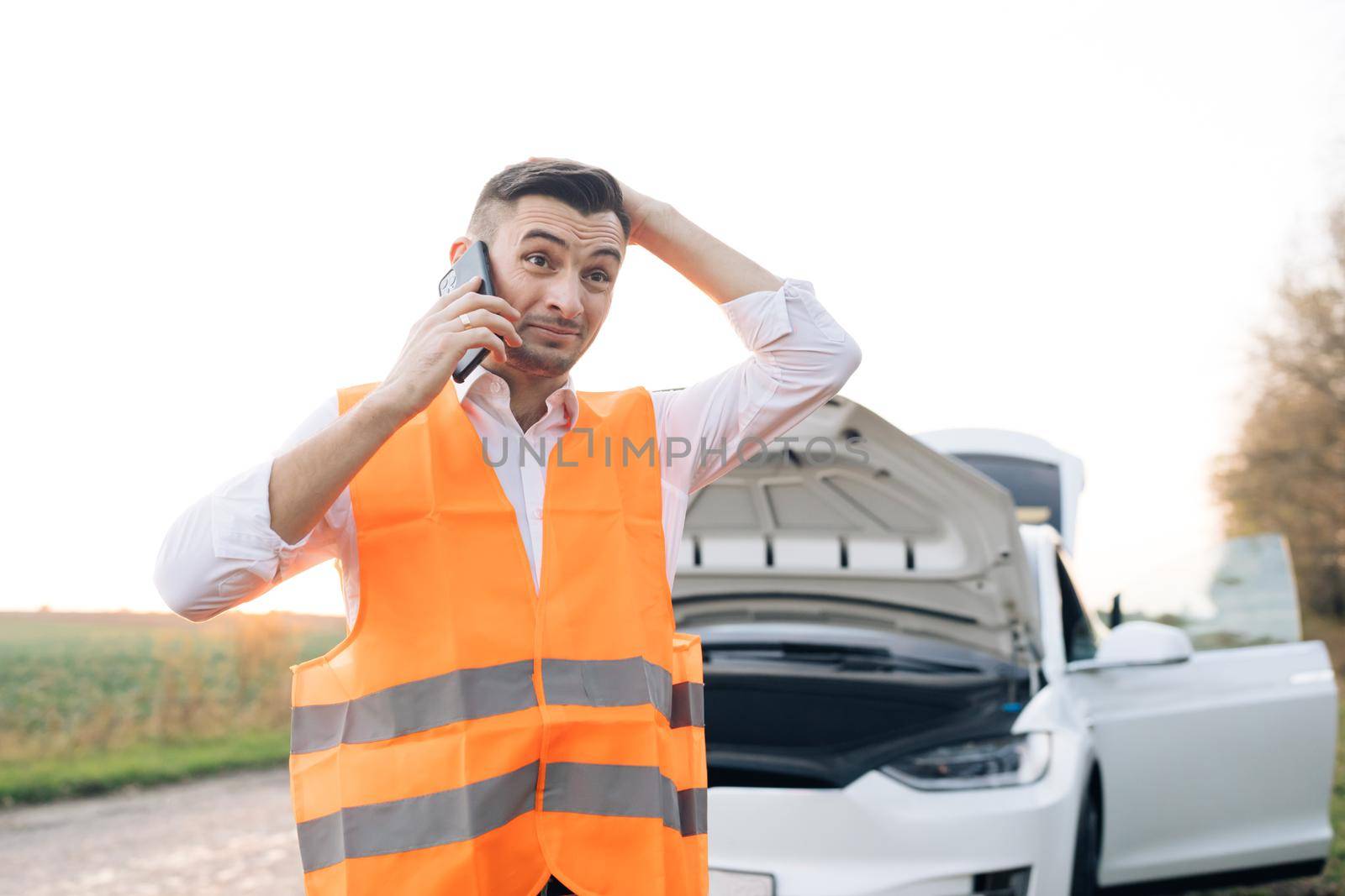 Man talking on the phone and looking at the car's engine. young man use smartphone, stading on road near the broken car opened the hood, calling car assistance services, help repair