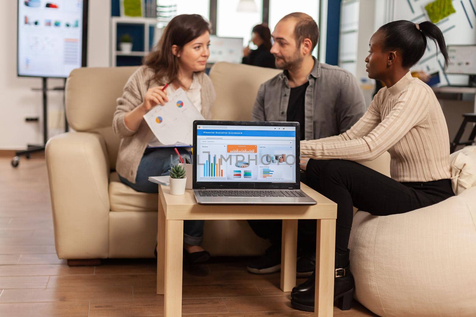 African woman talking about project, discussing start up ideas using laptop with graphics, diverse employees gathered in co-working process in company. Teamworkers helping each other finding strategy