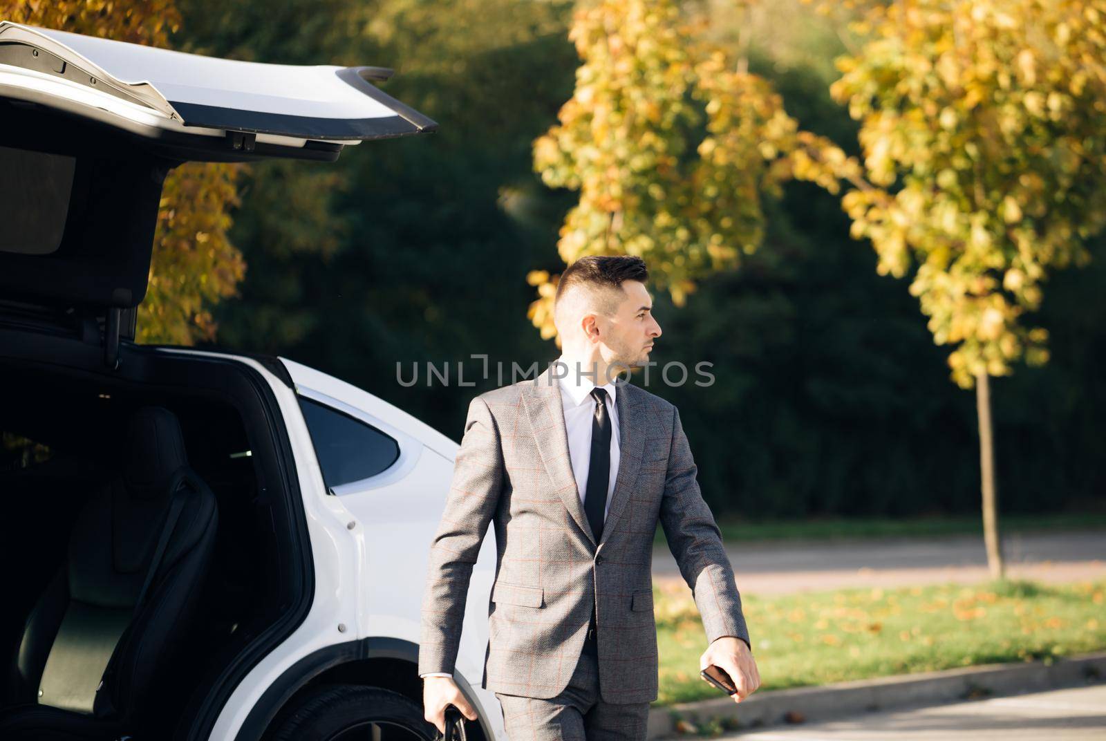 Stylish man getting out of car, personal chauffeur bringing businessman. Business man with briefcase get out from auto and walking to office building.