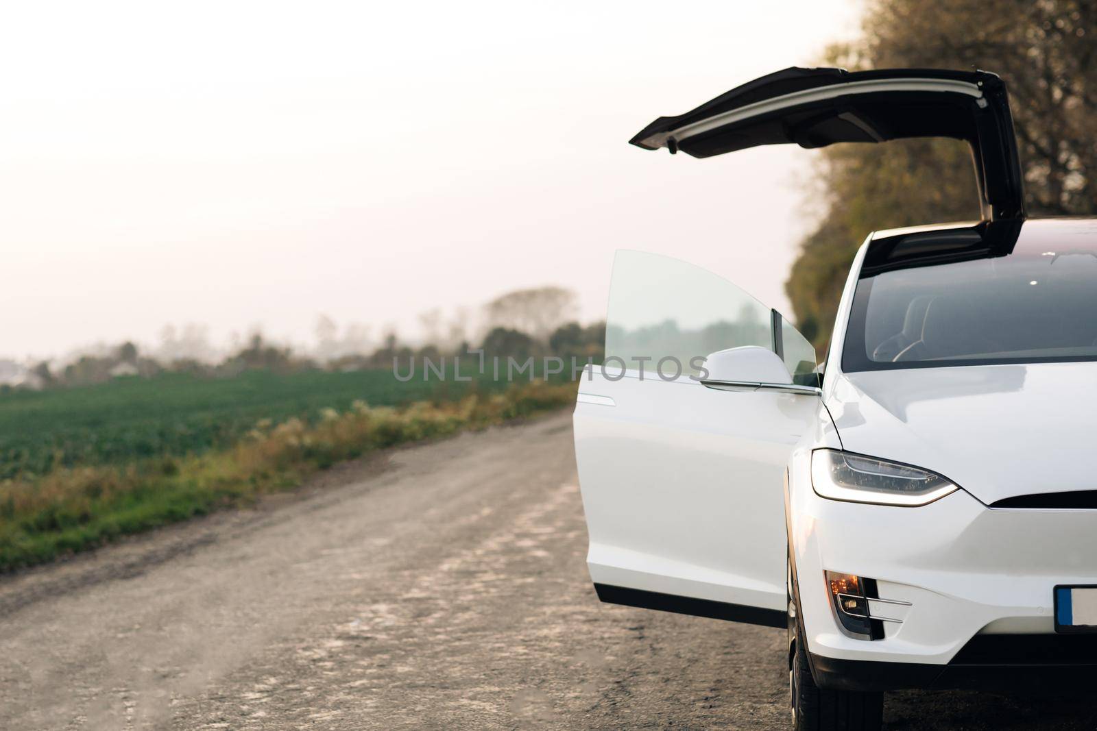 Luxury modern vehicle along trees and fields. Electric Car on Country Road. Electric Car on Gravel road with trees at sunset