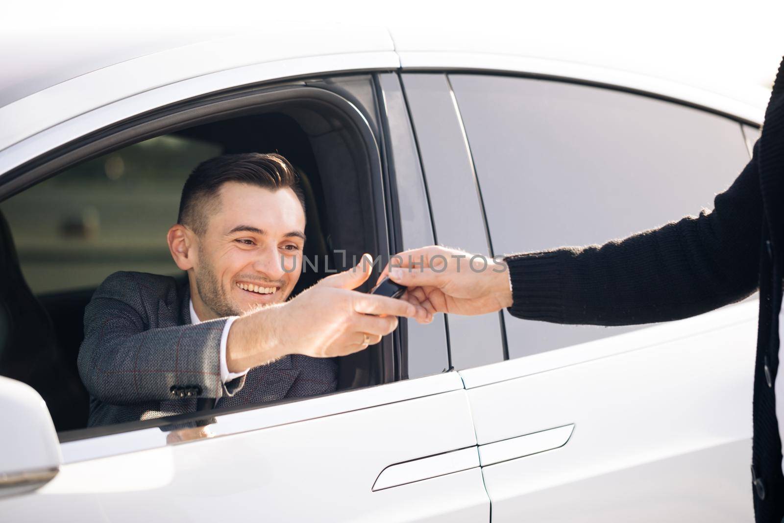 Young Happy Man Receiving Car Keys to Her New Automobile. Dealer giving key to new owner in auto show or salon. Car Salesman Finishing Up Dealing Car.