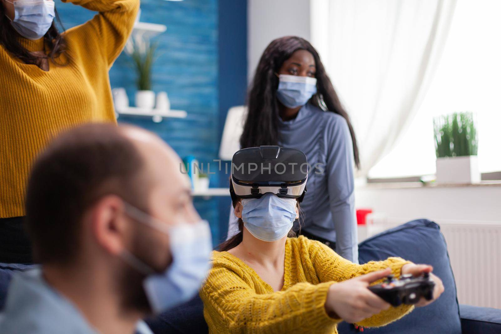Woman experiencing virtual reality playing video games wearing vr headset during social pandemic with friends in home living room respecting social distancing having face mask not to spread the virus.