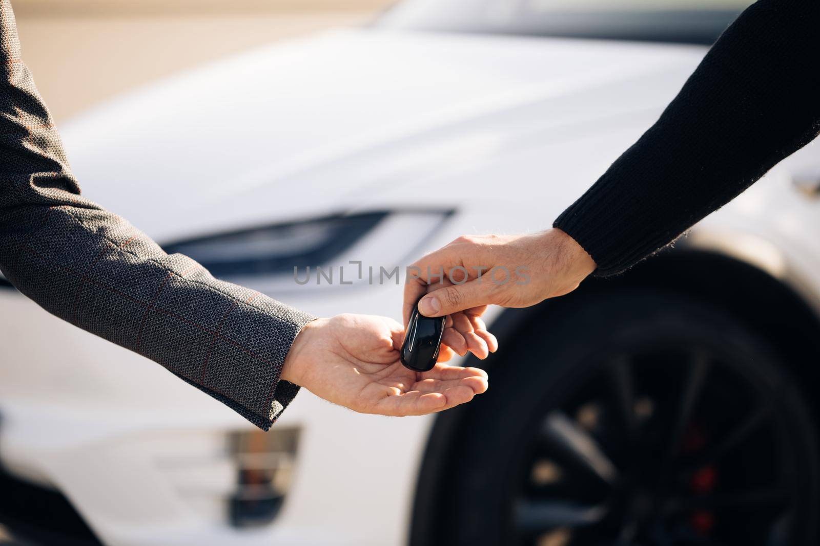 Car Salesman Finishing Up Dealing Car. Young Happy Man Receiving Car Keys to Her New Automobile. Dealer giving key to new owner in auto show or salon