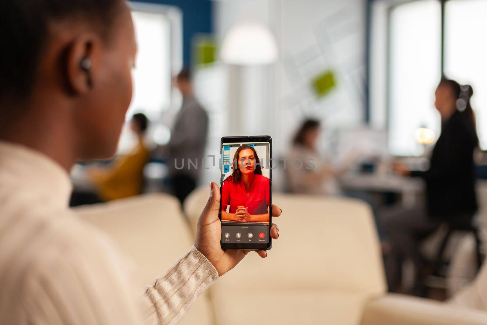 Over the sholder of black employee discussing with partner on video call using phone in start up business office. Black woman during video meeting, online conferencel planning new financial project
