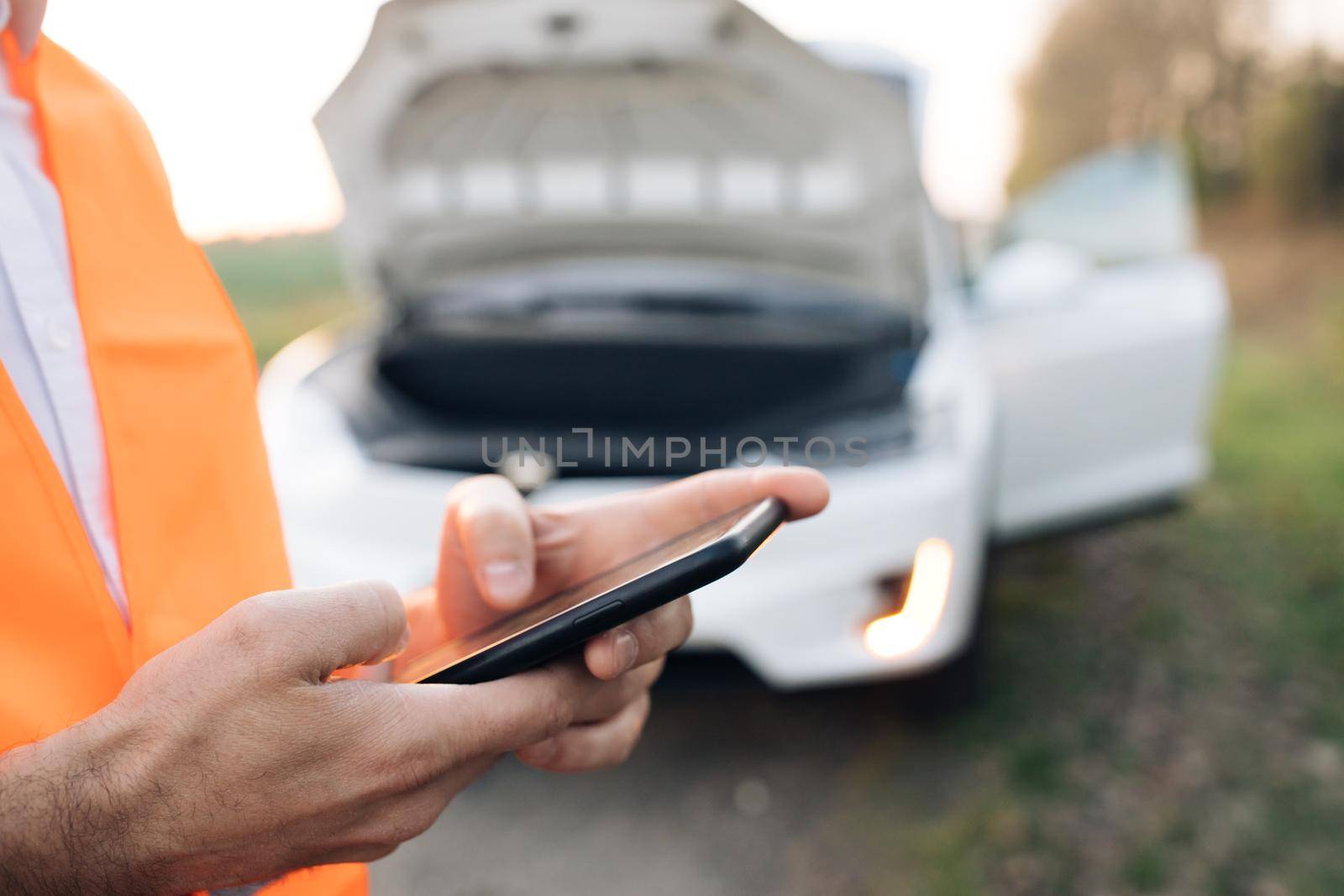 The man is using the phone in asking for help when his electric car is broken. Man in a safety vest. Concept road accident. Help repair.