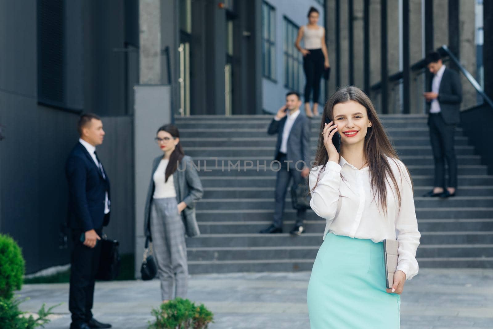 Beautiful young businesswoman wearing white shirt using modern smart phone. Professional female employer typing text message on cellphone outside by uflypro