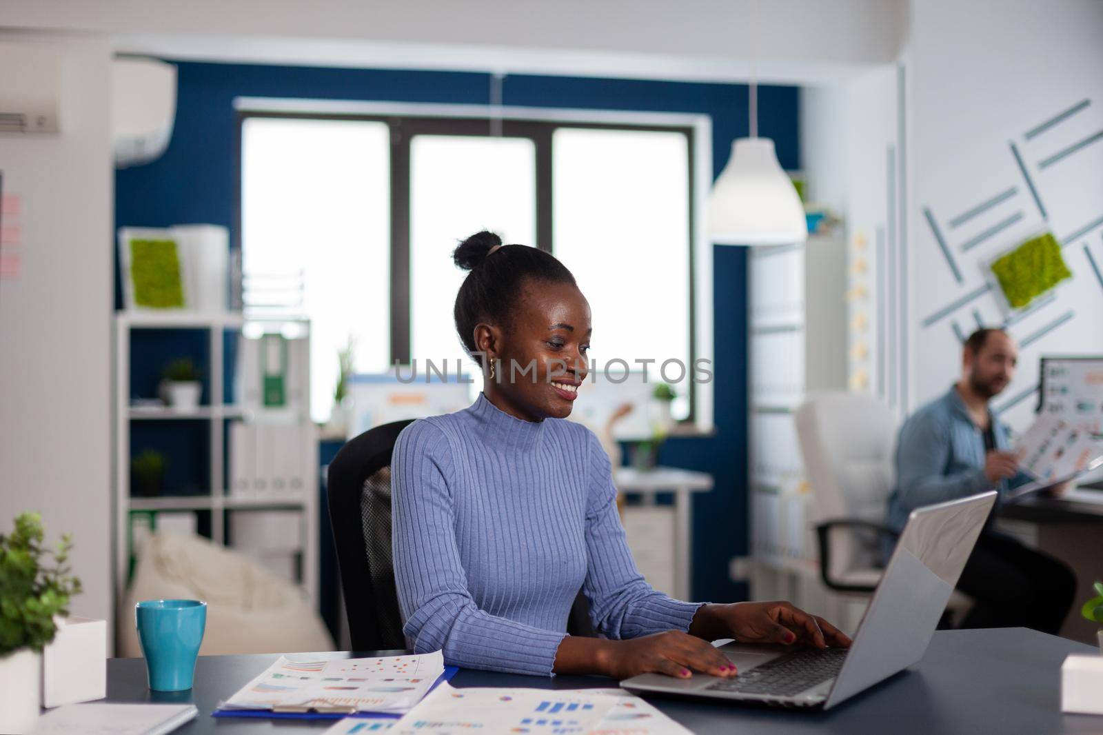 African woman working typing on laptop computer, concentrated to finish important deadline. Diverse team of business people analyzing company financial reports from computer.