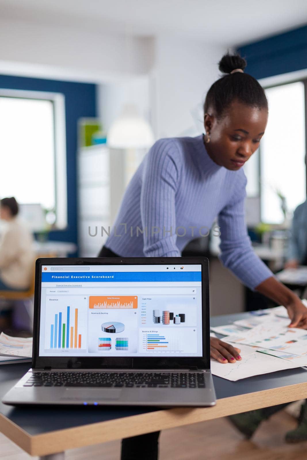 Laptop with financial charts on office of start up company and african woman reading statistics. Diverse team of business people analyzing company financial reports from computer. Successful corporate professional entrepreneur online internet statistics