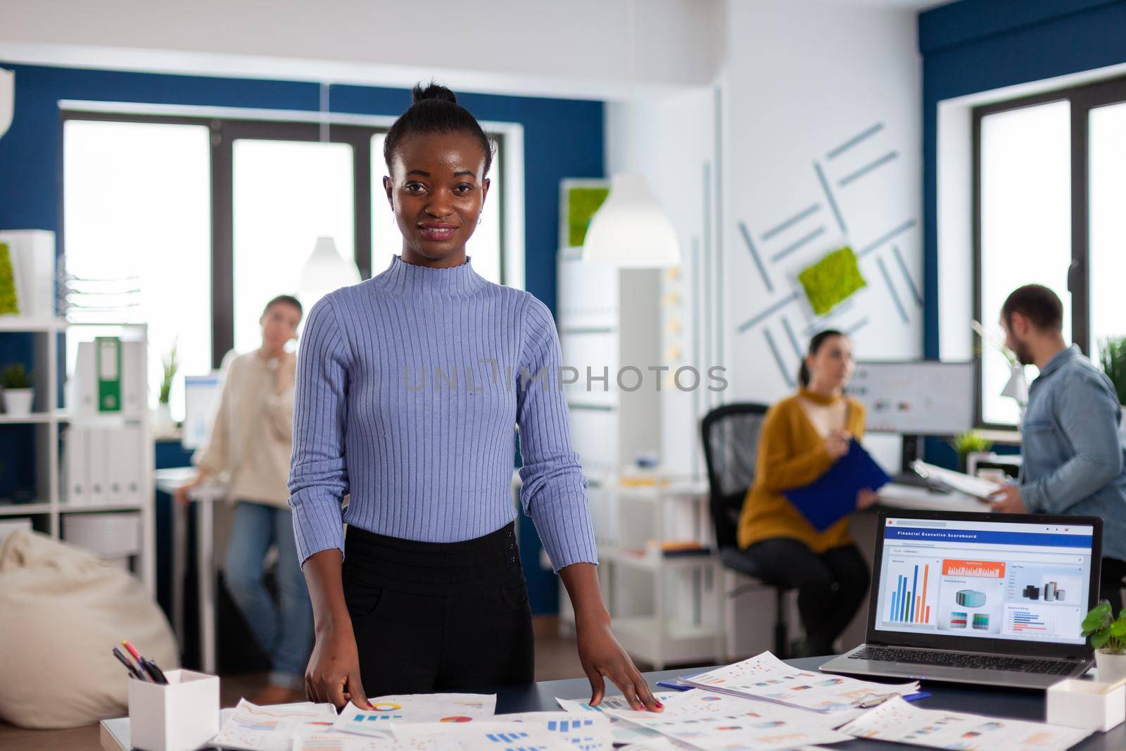 Black woman entrepreneur looking at camera with business people working on project strategy. Diverse team of business people analyzing company financial reports from computer.