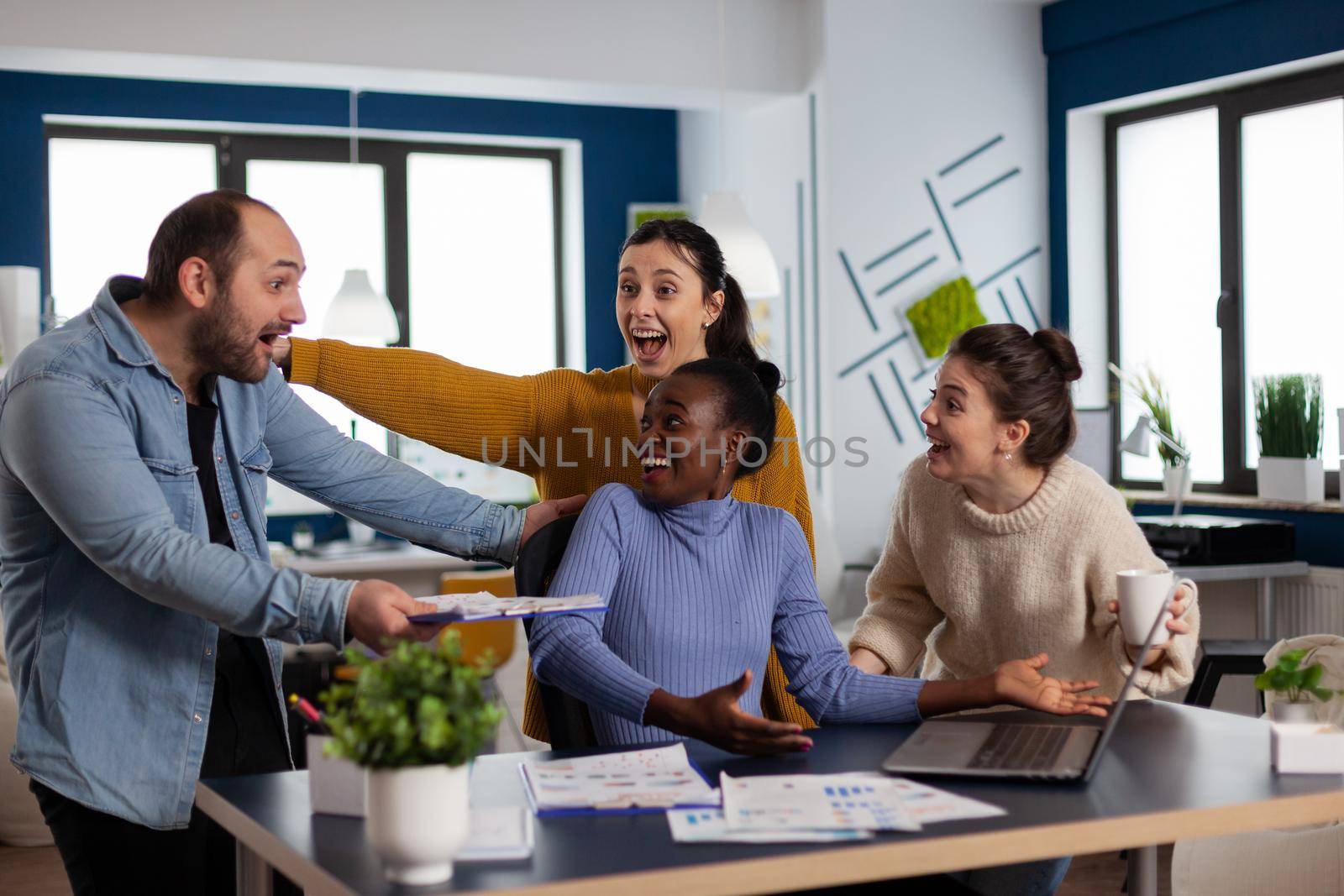 African manager and coworkers looking surprised celebrating succes of company triumph. Multiethnic diverse business team with laptop and papers excited about project.