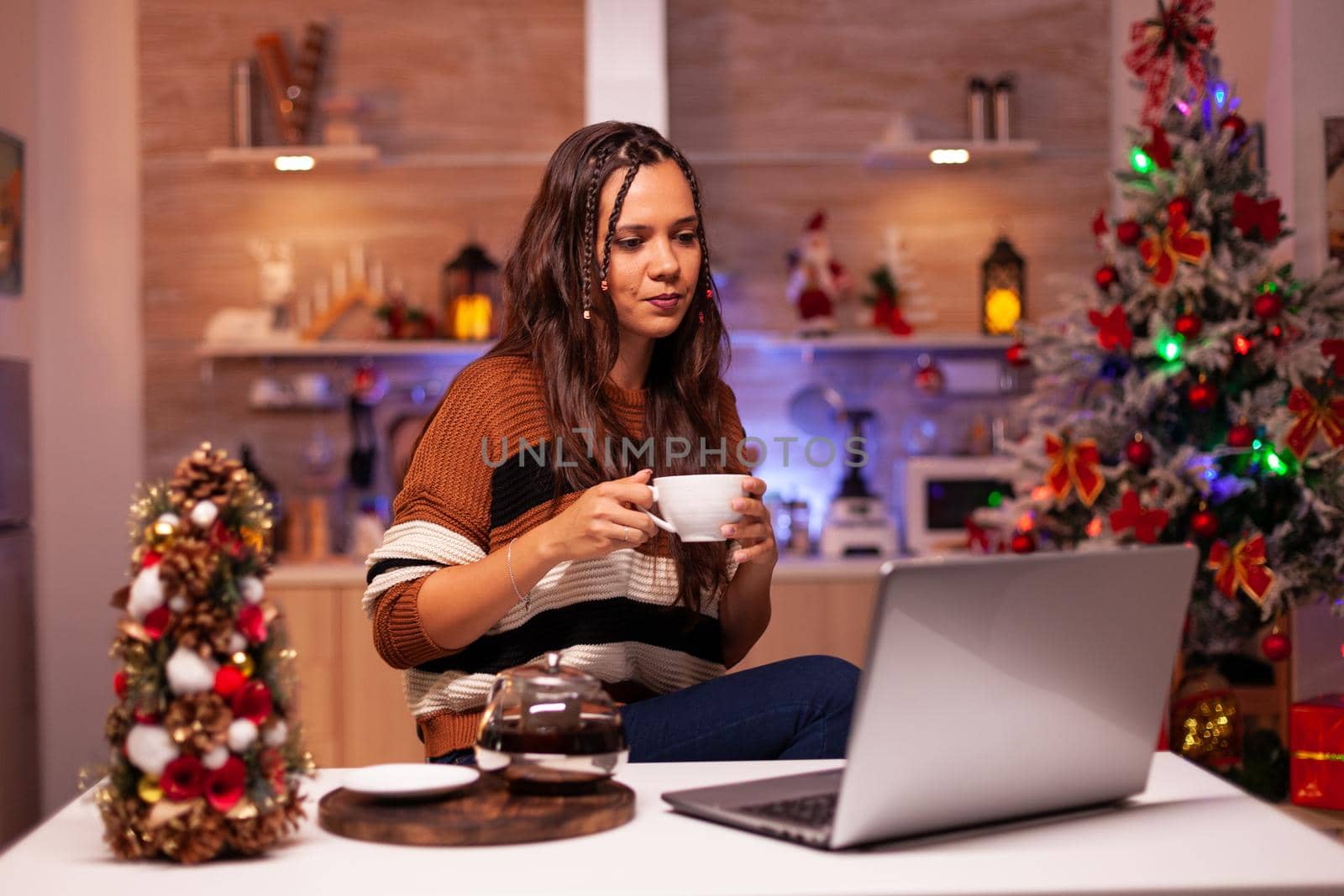 Traditional person on video call conference on internet in seasonal decorated kitchen. Festive woman chatting to friends and relatives on laptop computer for winter celebration at home