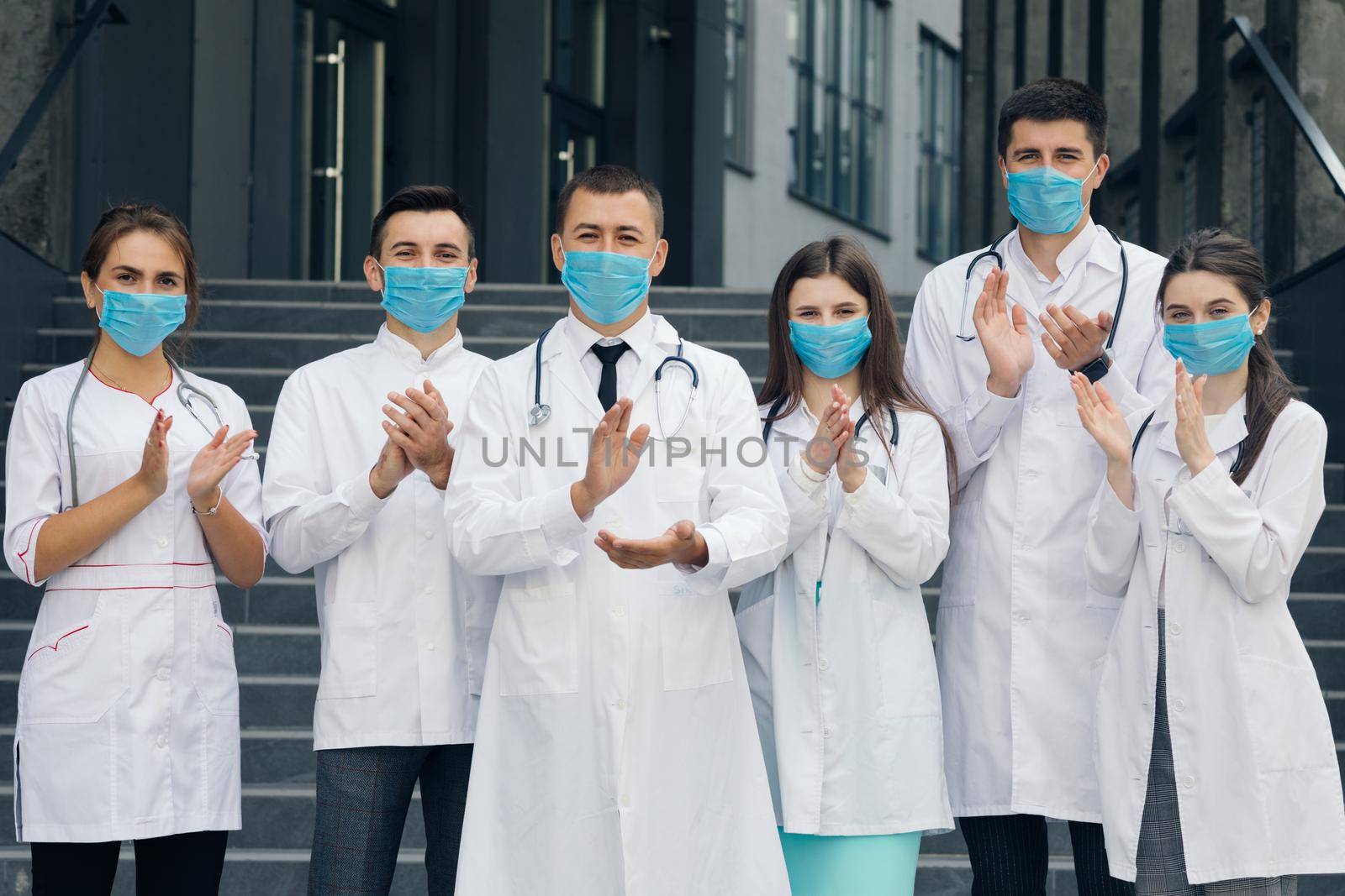 Medical staff from the hospital who are fighting coronavirus applaud back the people and police officers for their support. Group of doctors with face masks. Corona Virus and Healthcare Concept by uflypro