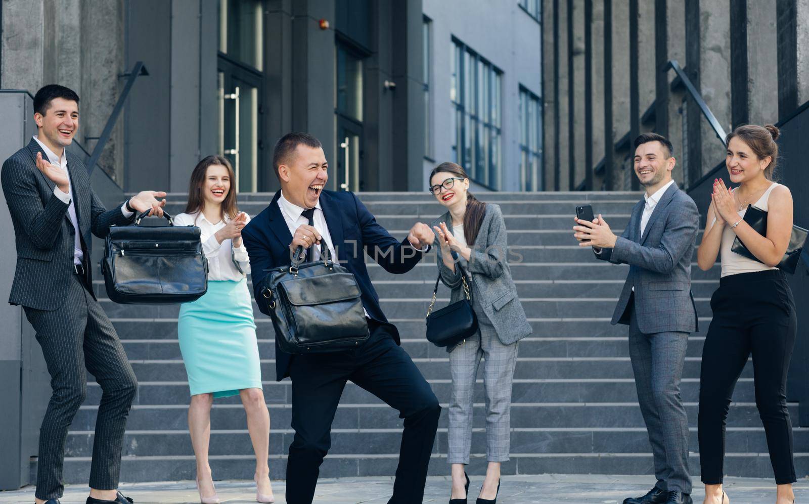 Overjoyed excited male leader and carefree business team dance together, happy staff group enjoy fun celebrate success victory concept by uflypro
