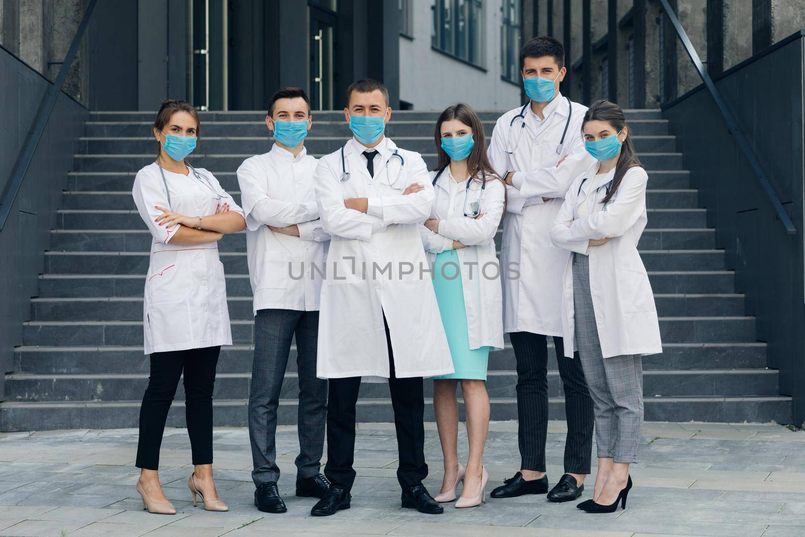 Doctors stand with arms crossed while wearing protective face masks outdoors during COVID-19 epidemic and Looking at Camera.
