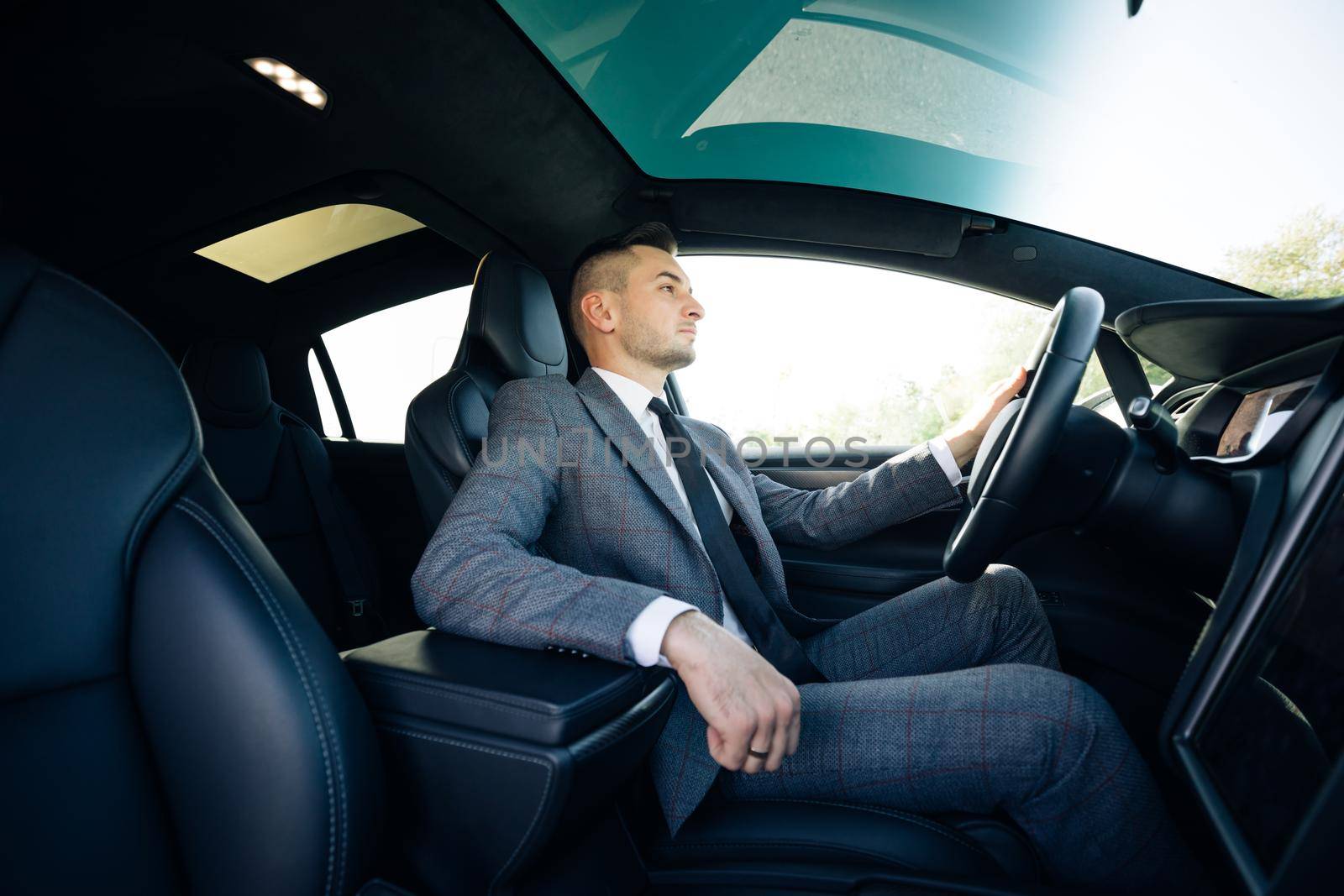 Portrait of male businessman sitting at the wheel of a car. Young cheerful man sitting in modern luxurious car staying in city center.