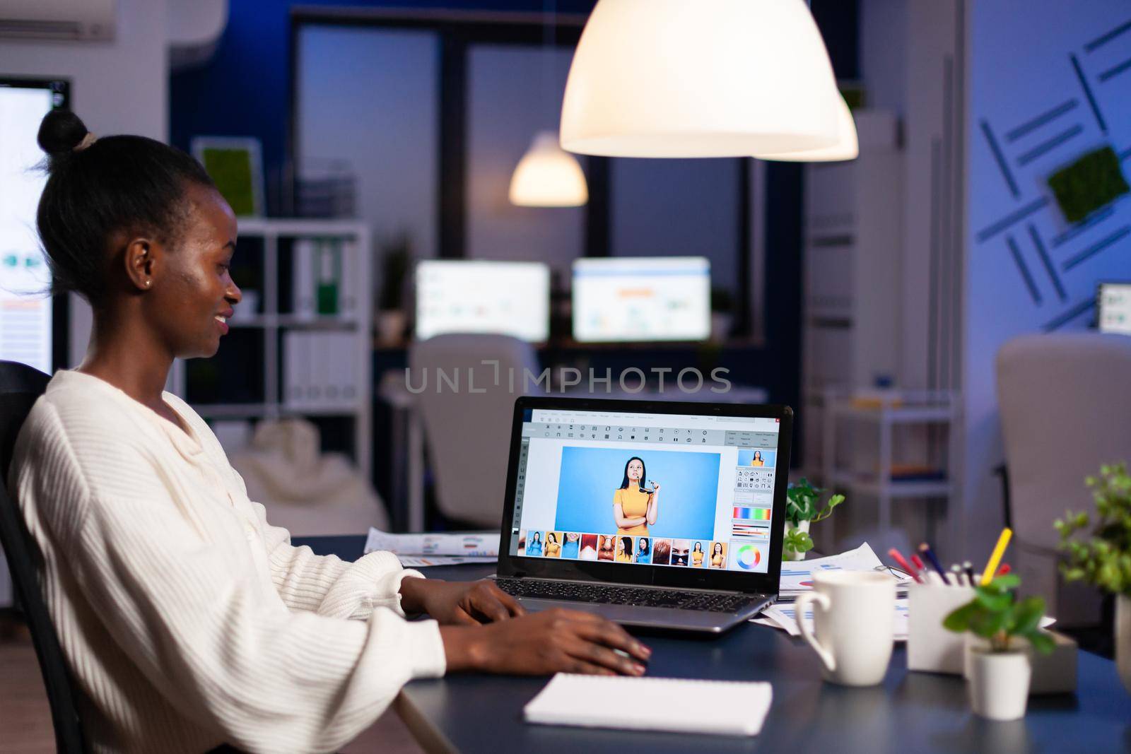 African professional woman photo retoucher working on laptop at new project in business office at night time. Content creator doing portrait retouching, artist, occupation, screen, graphic.