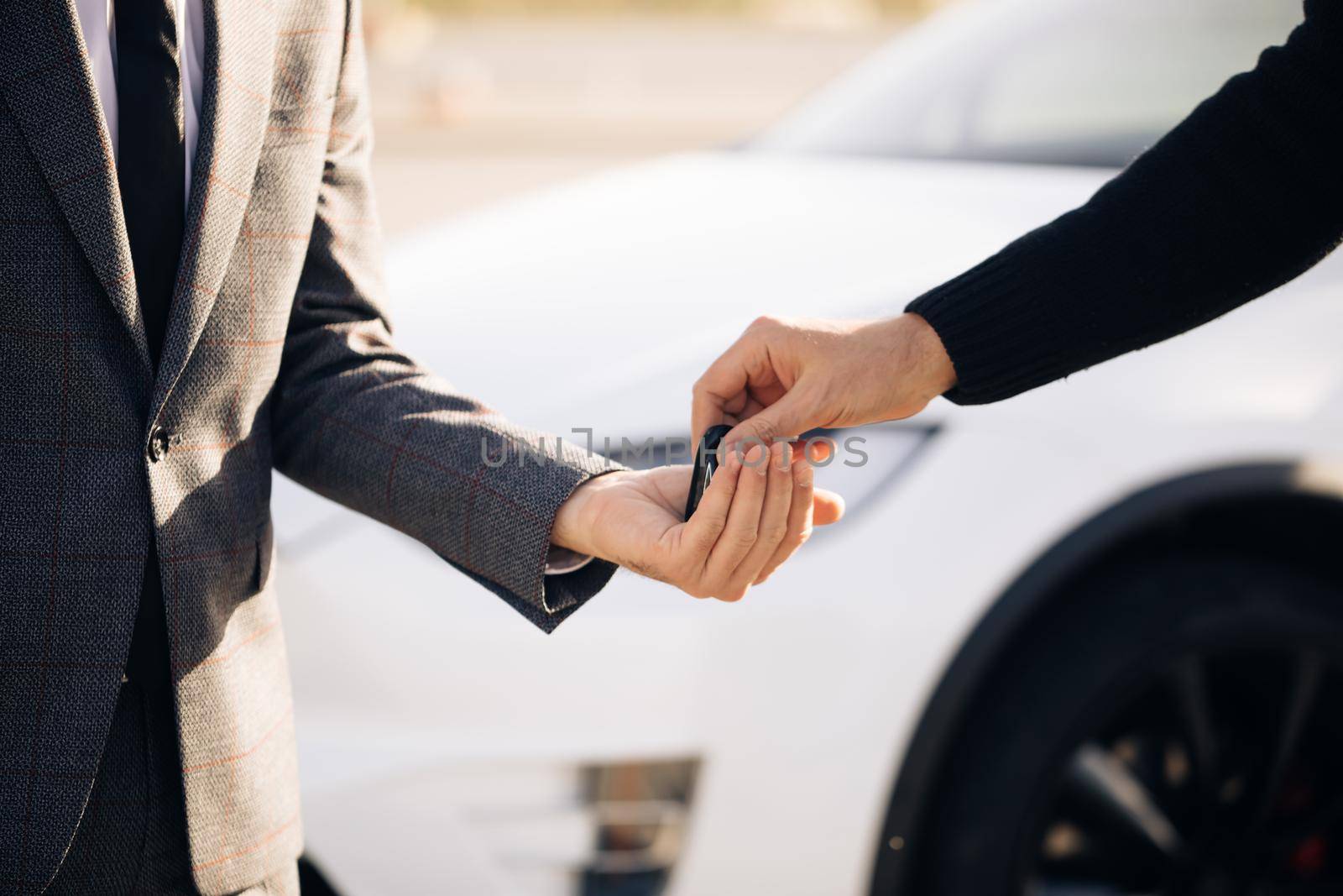 Male hand gives a car keys to male hand in the car dealership close up. Unrecognized auto seller and a man who bought a vehicle. Dealer giving key to new owner in auto show or salon by uflypro