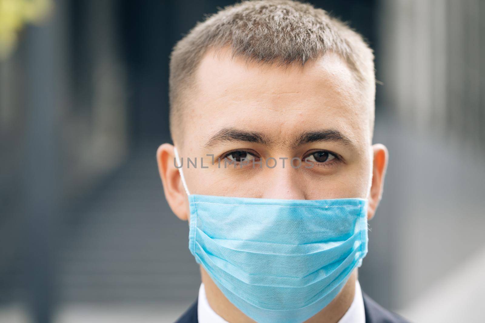 Close up of face of young handsome businessman in medical mask looking straight to camera with happy look. Portrait of man at street. Coronavirus concept by uflypro