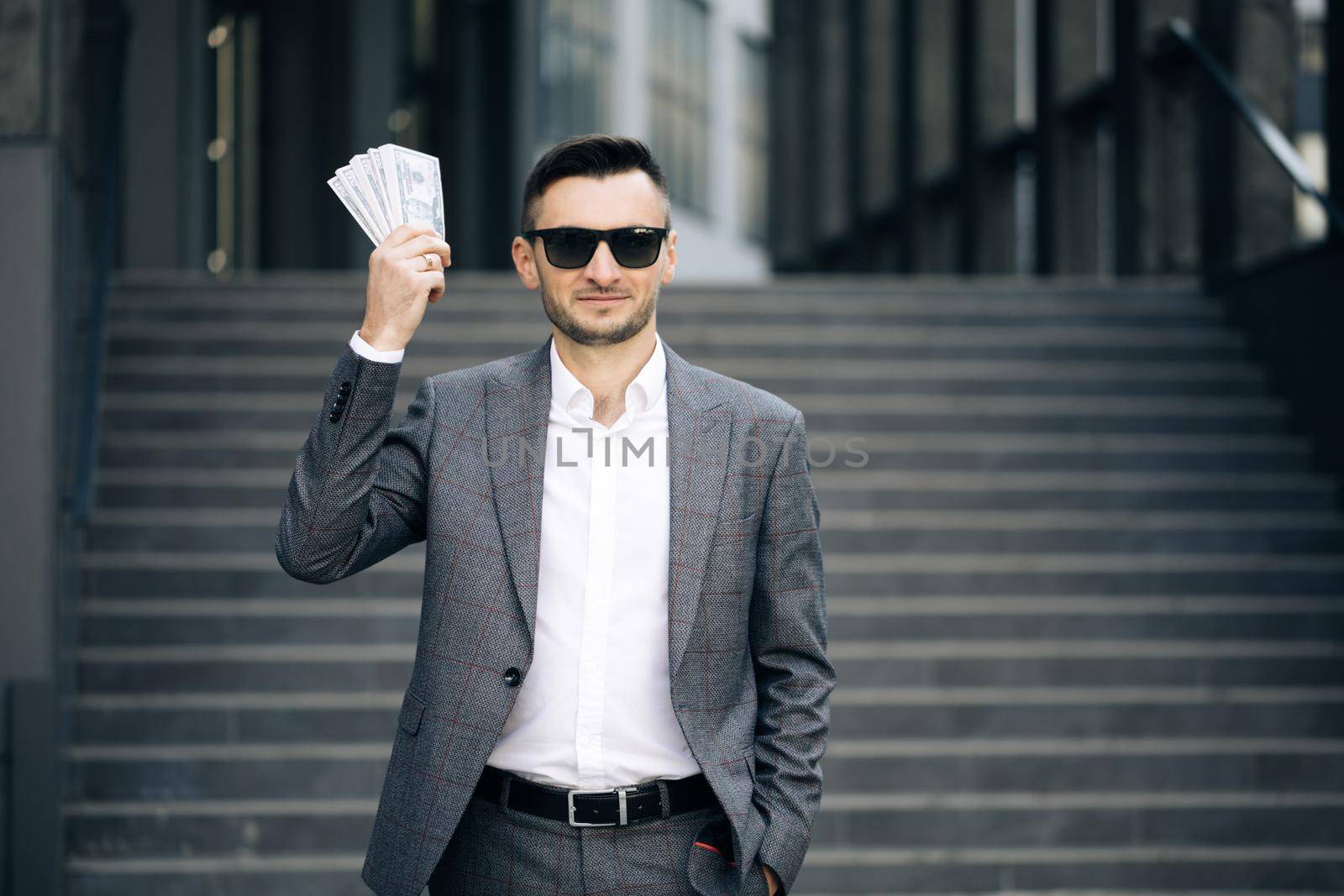 Lifestyle, richness, joy, success. Happy rich successful man holds dollars outdoors. Portrait of satisfied businessman holds money. by uflypro