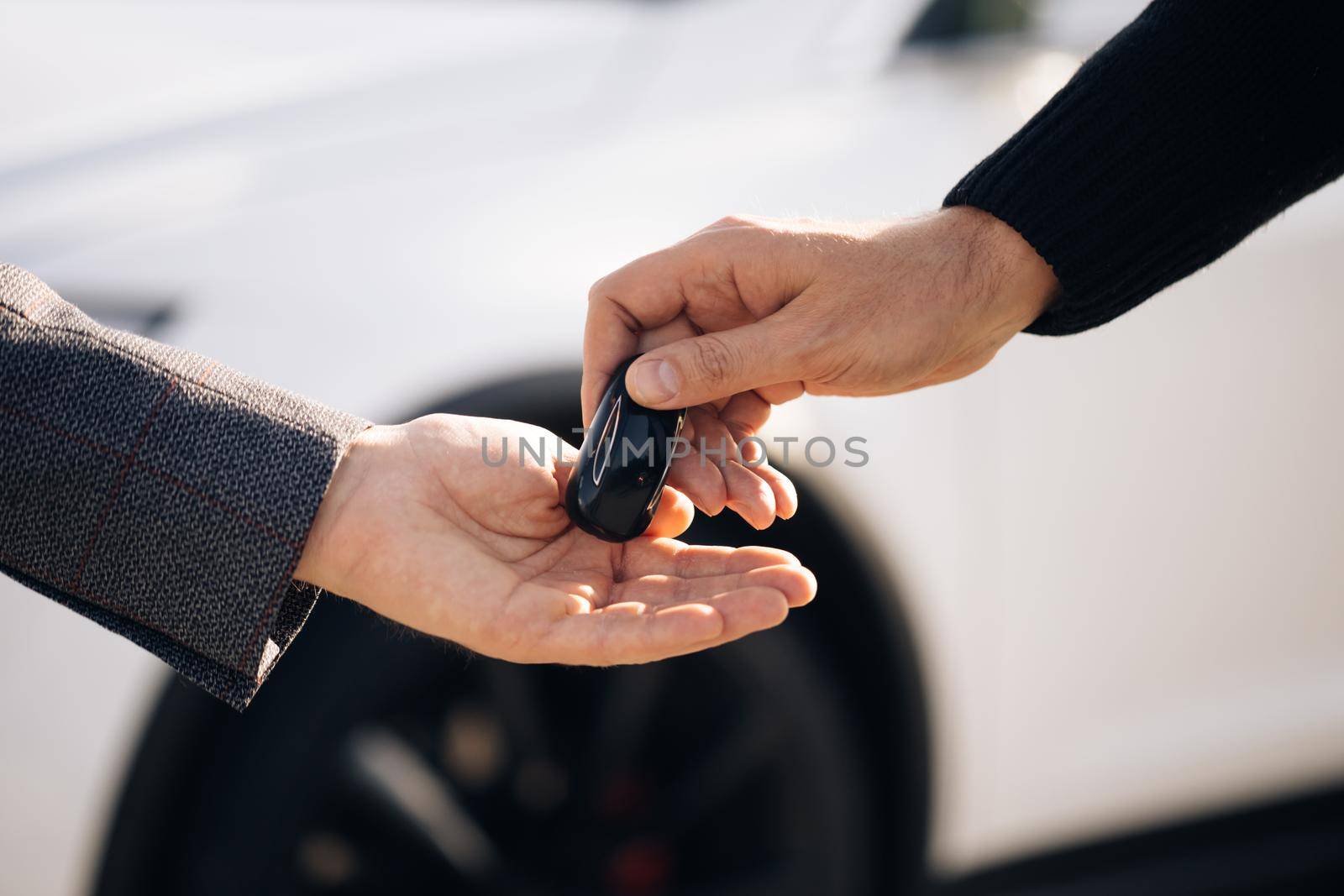 Dealer giving key to new owner in auto show or salon. Male hand gives a car keys to male hand in the car dealership close up. Unrecognized auto seller and a man who bought a vehicle