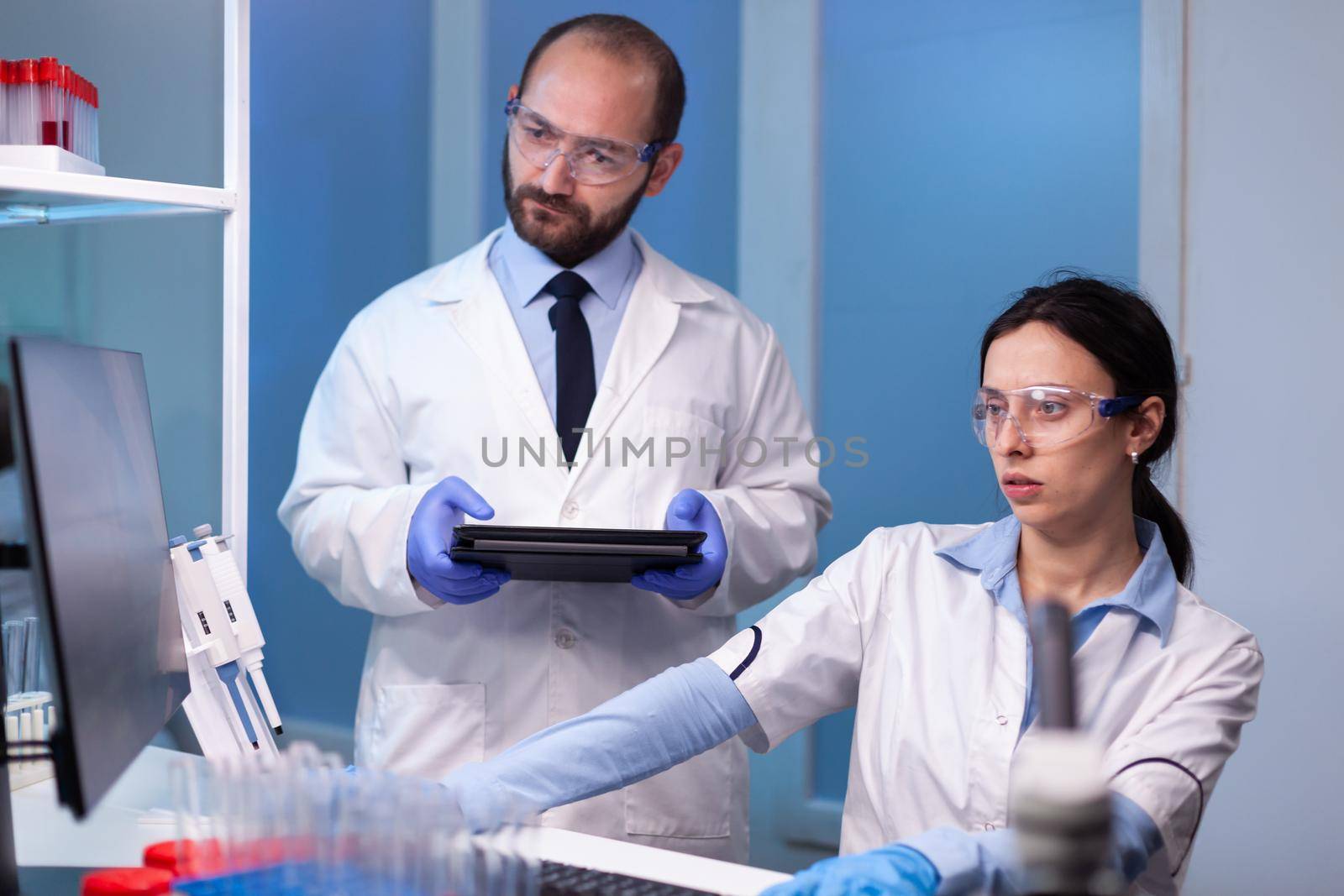Professional team of medical researchers working together in sterile lab wearing protection glasses and white coat. Biochemist doctors analysing a medical experiment to discover a vaccine